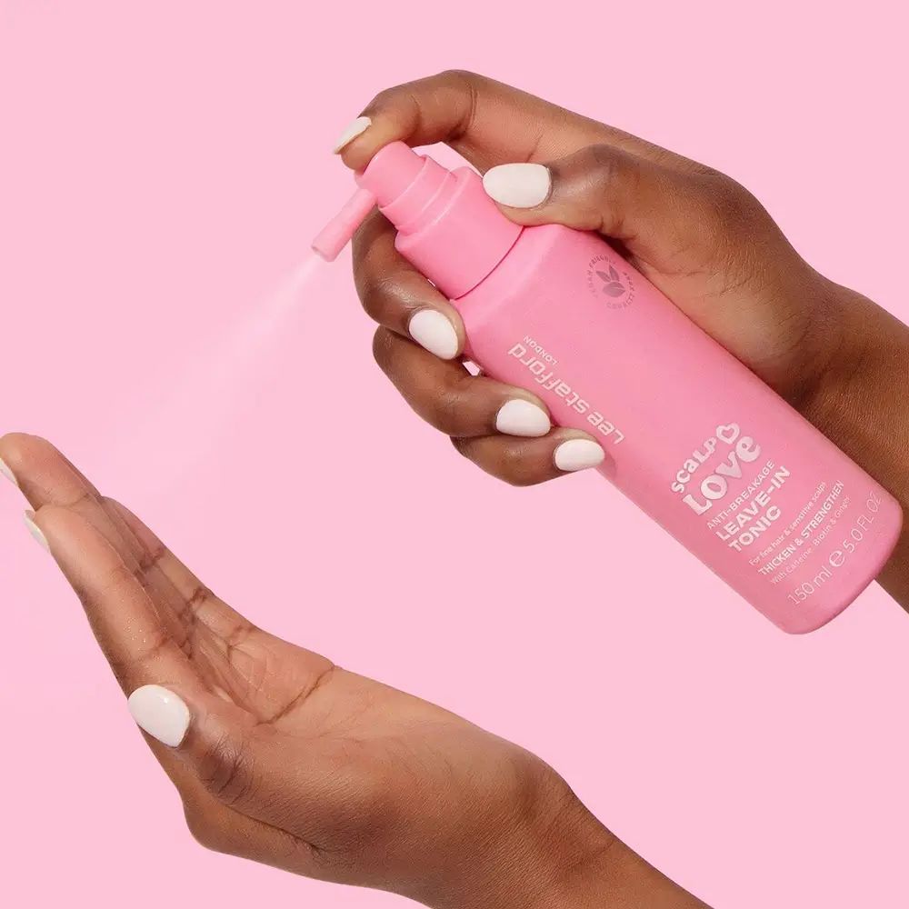 Mani che tengono flacone rosa con erogatore spray. Nebbia spray visibile. Scritta: Scalp Love. Marchio: Lee Stafford. Logo vegan.