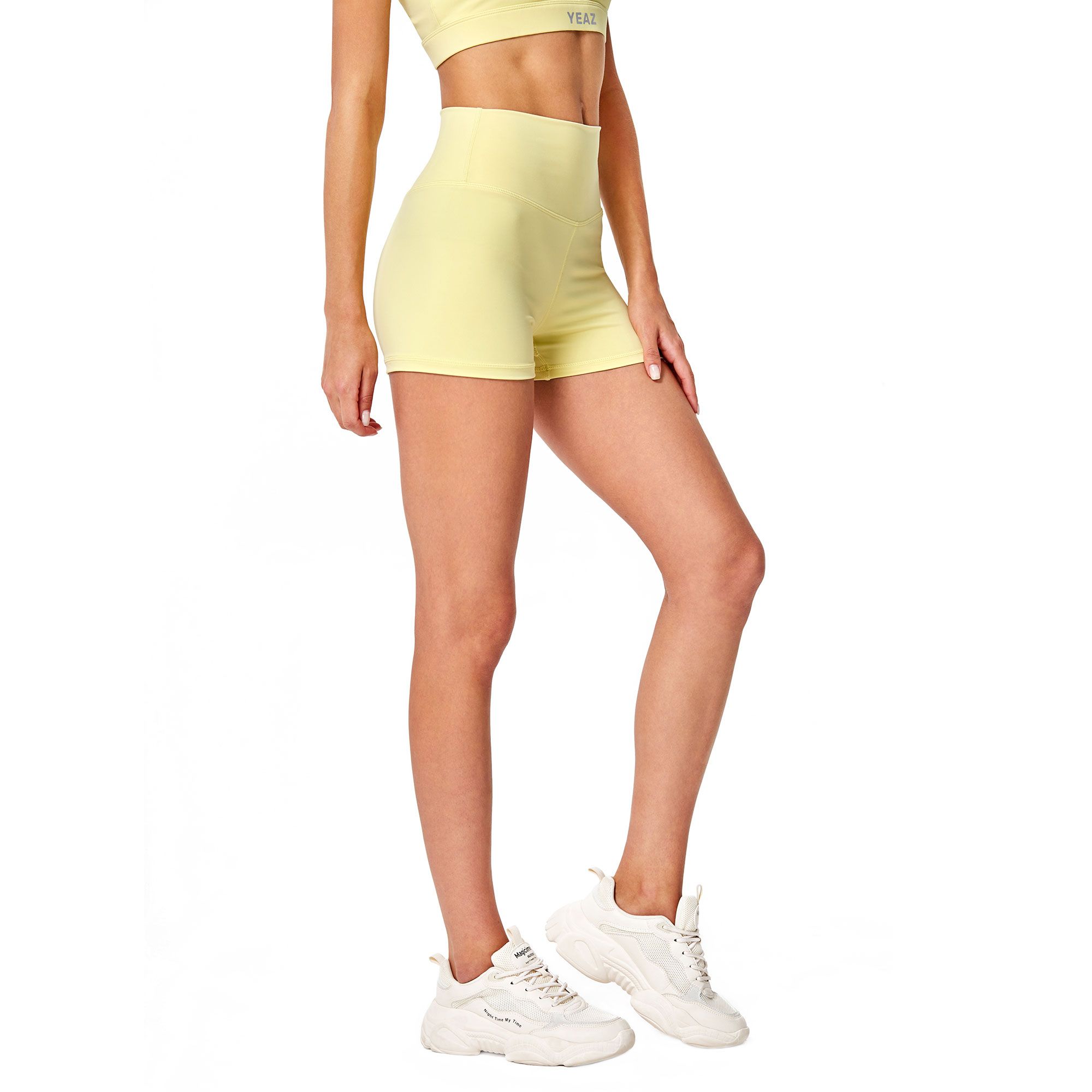 Una donna indossa pantaloncini gialli aderenti e un reggiseno sportivo abbinato. Scarpe da ginnastica bianche completano l'outfit.