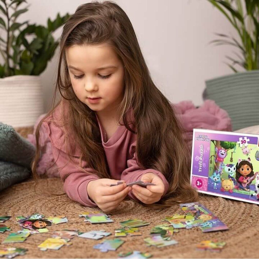 Bambina che fa un puzzle. Puzzle con Gabby e personaggi di gatti. Pezzi del puzzle sul pavimento. Confezione sullo sfondo.
