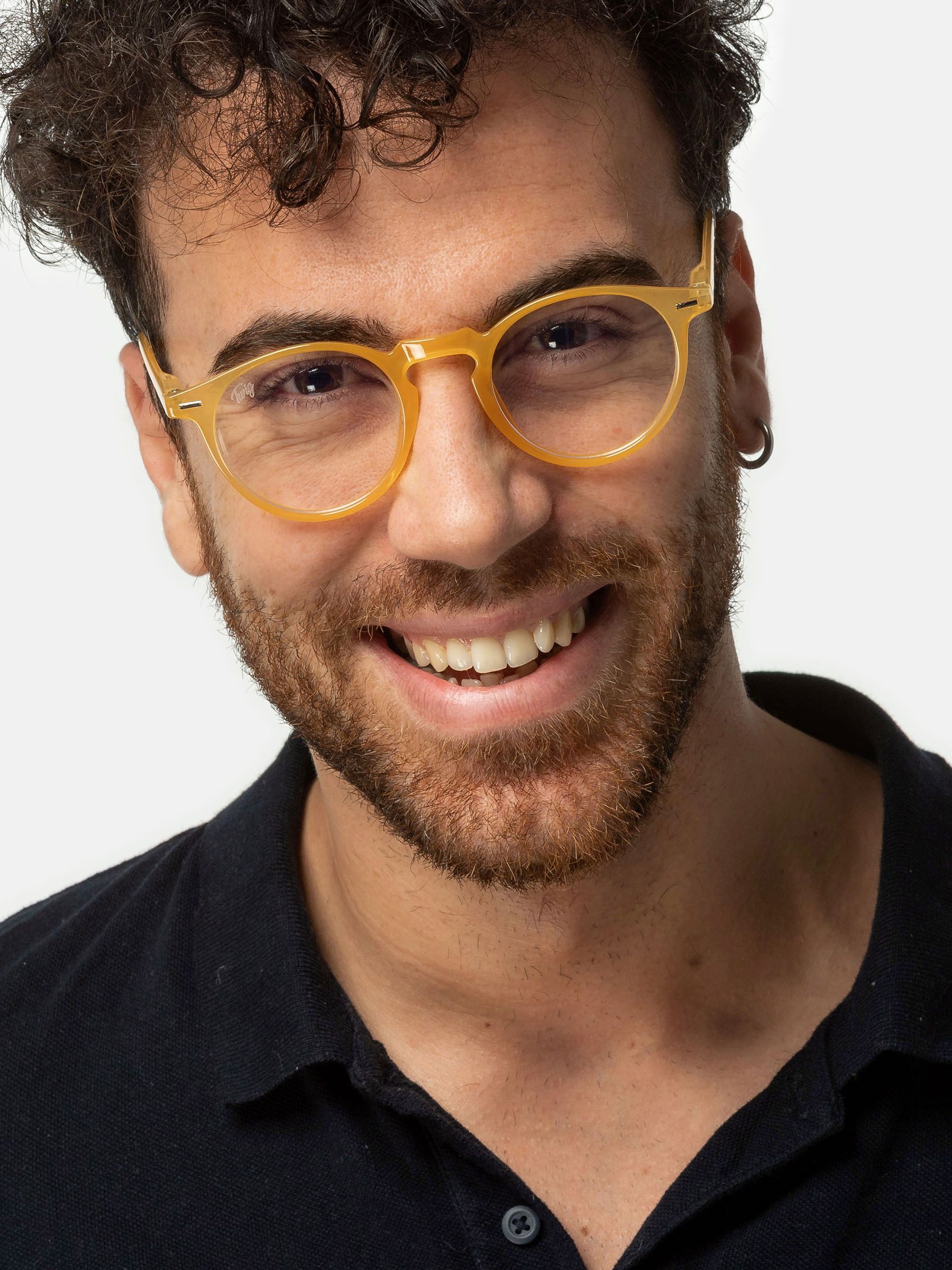 Uomo con occhiali gialli. Lenti rotonde, montatura gialla. Sorride. Camicia scura.