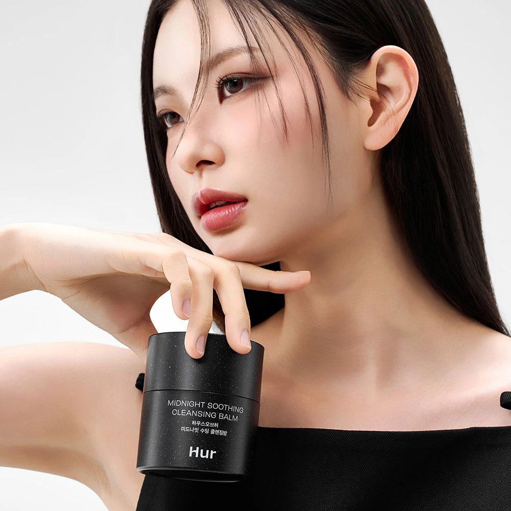 Persona che tiene un barattolo nero. Scritta: Midnight Soothing Cleansing Balm. Marchio: Hur. Sfondo bianco.