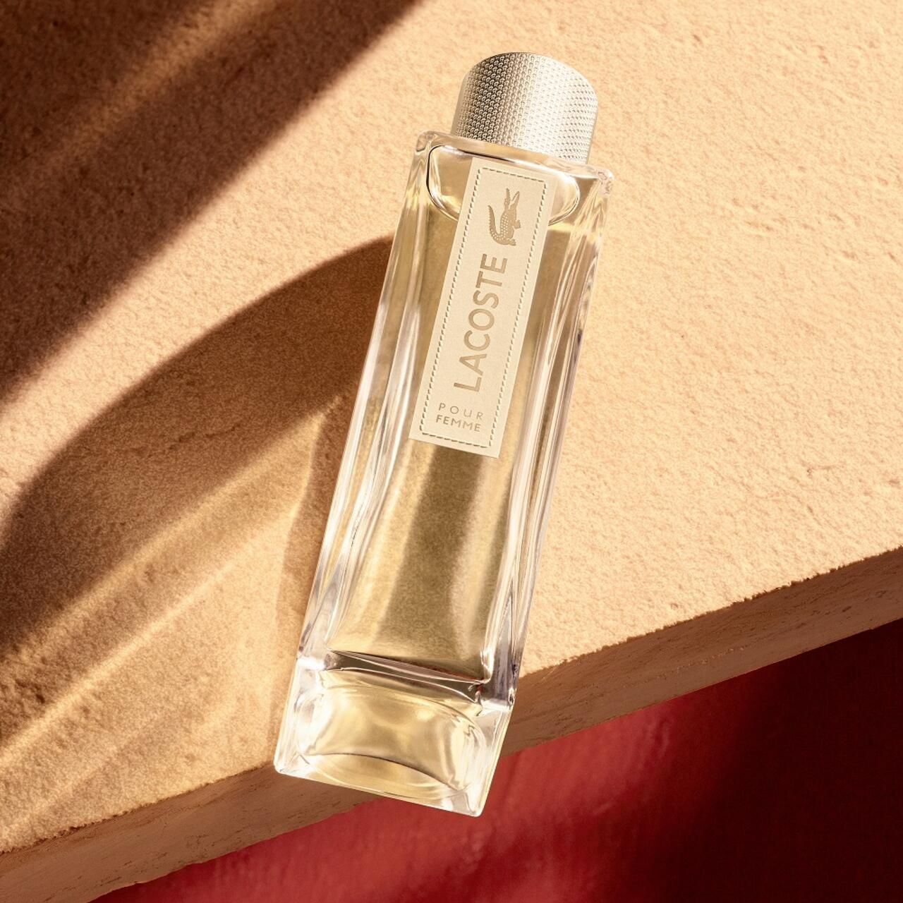 Flacone di profumo su una superficie. L'etichetta riporta "Lacoste Pour Femme".