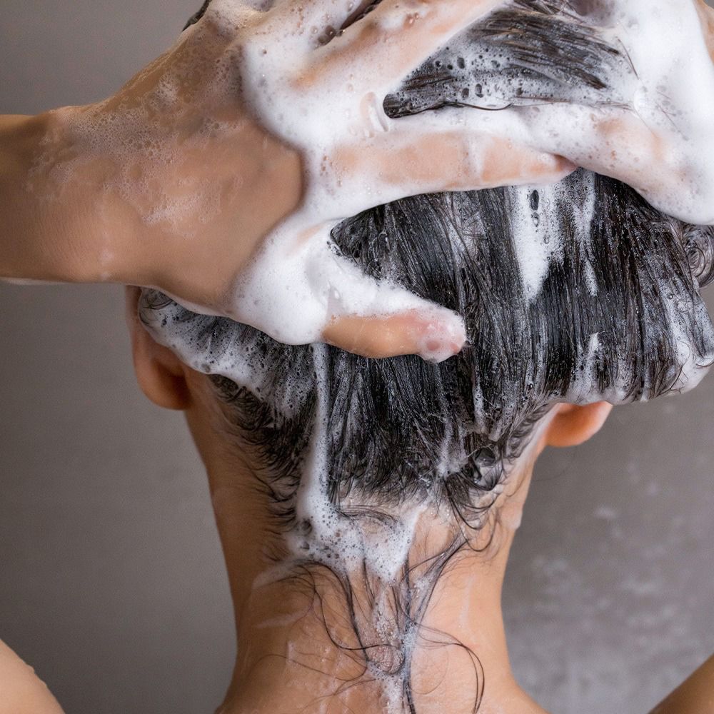 Mani che lavano i capelli con schiuma. Vista posteriore di una persona.