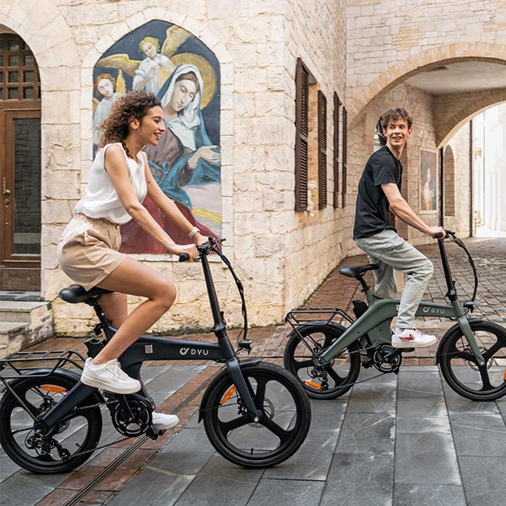 Due persone in sella a e-bike DYU grigie e verdi. Edificio sullo sfondo. Logo DYU visibile.
