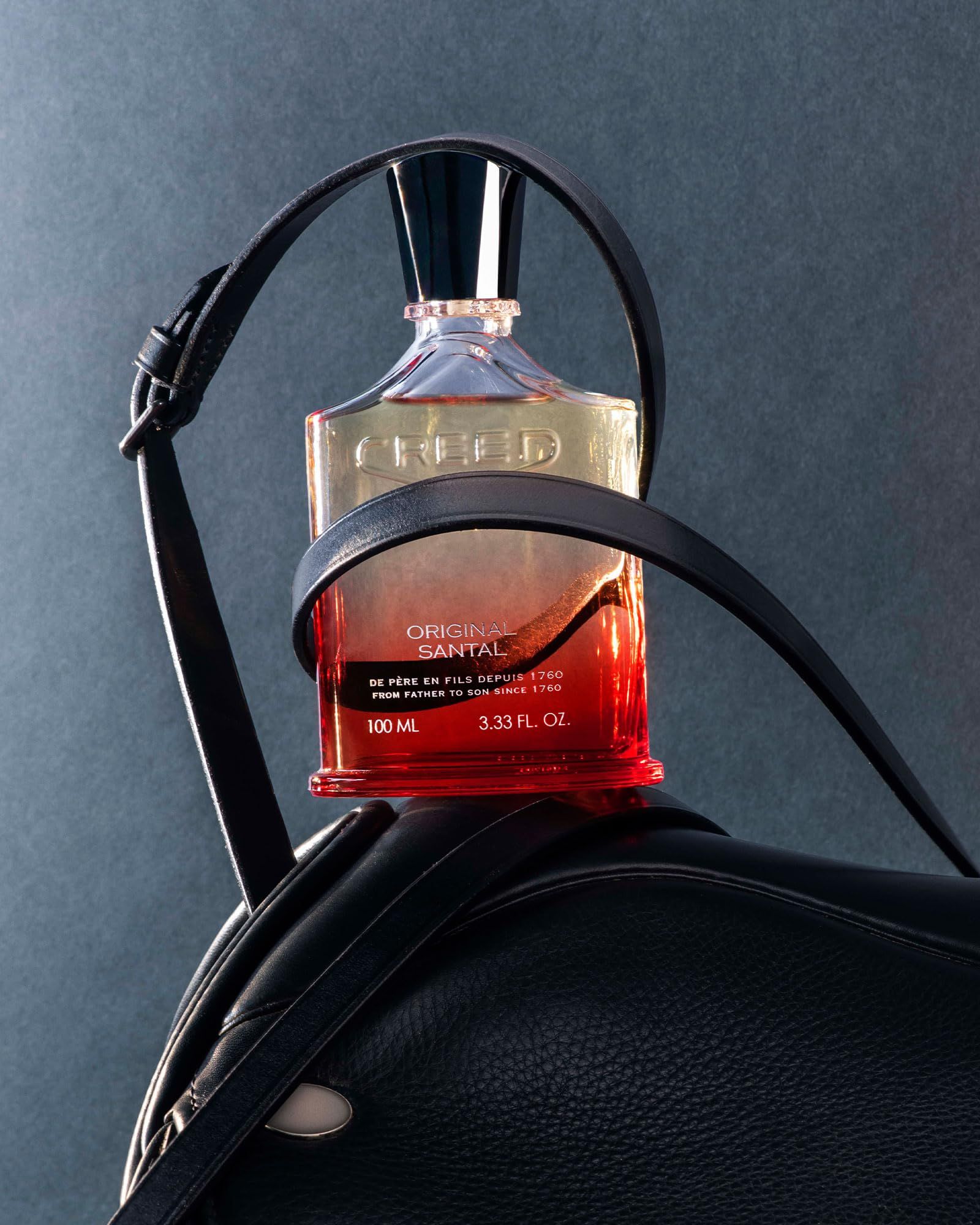 Flacone di profumo sfumato su una sella. Scritta: CREED ORIGINAL SANTAL.