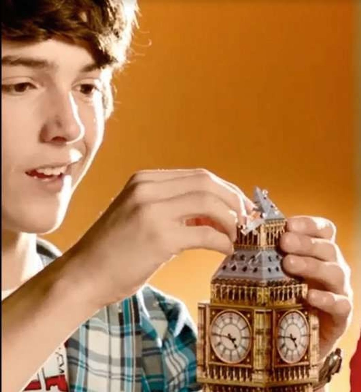 Ragazzo che assembla un pezzo del Big Ben. Elementi dorati e grigi. Meccanismo dell'orologio visibile. Sfondo arancione.