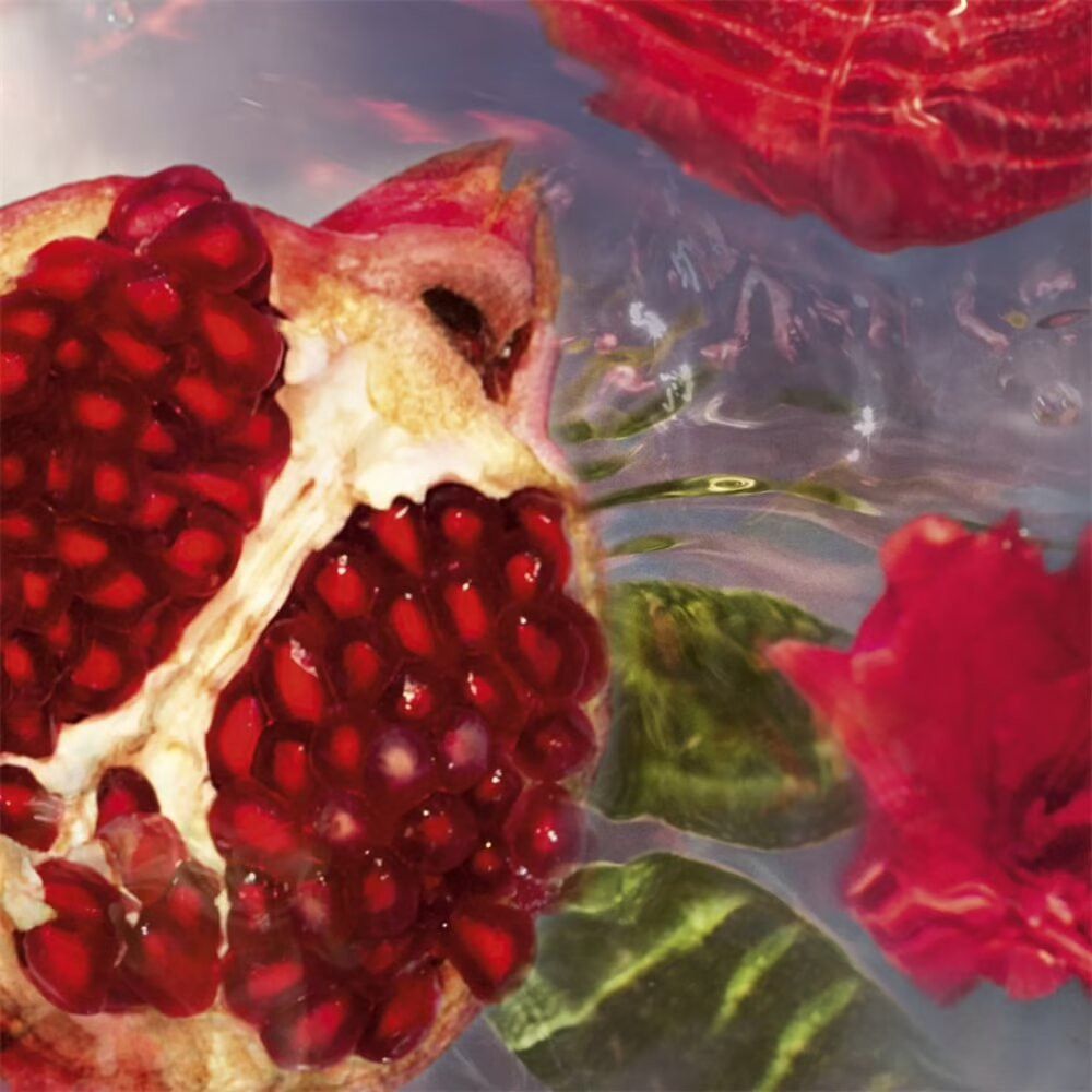 Metà melograno con semi rossi, circondato da acqua e petali rossi. Primo piano.