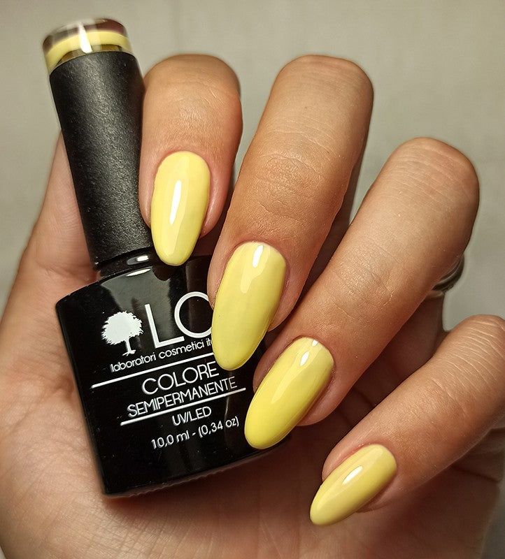 Mano con unghie smaltate e flacone di smalto. Unghie gialle e flacone di smalto nero con logo e testo bianchi.