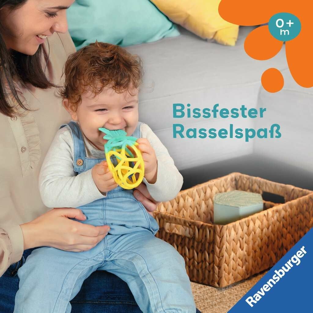 Bambino con massaggiagengive a forma di ananas in bocca. Forma giallo-turchese. Bambino sulle ginocchia di una persona. Cesto sullo sfondo.