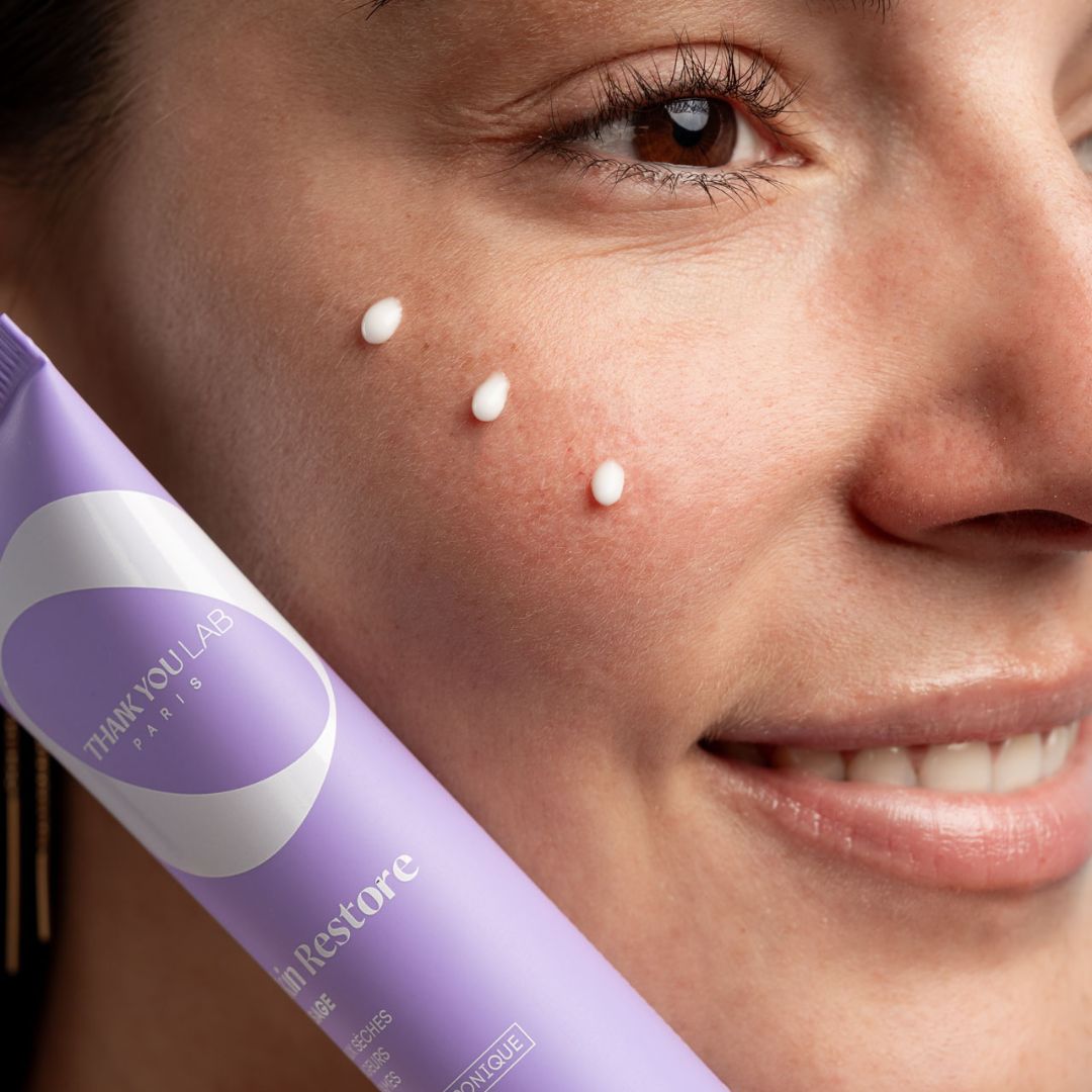 Tubo lilla con crema bianca. Tre punti di crema sulla pelle. Scritta: THANK YOU LAB PARIS.