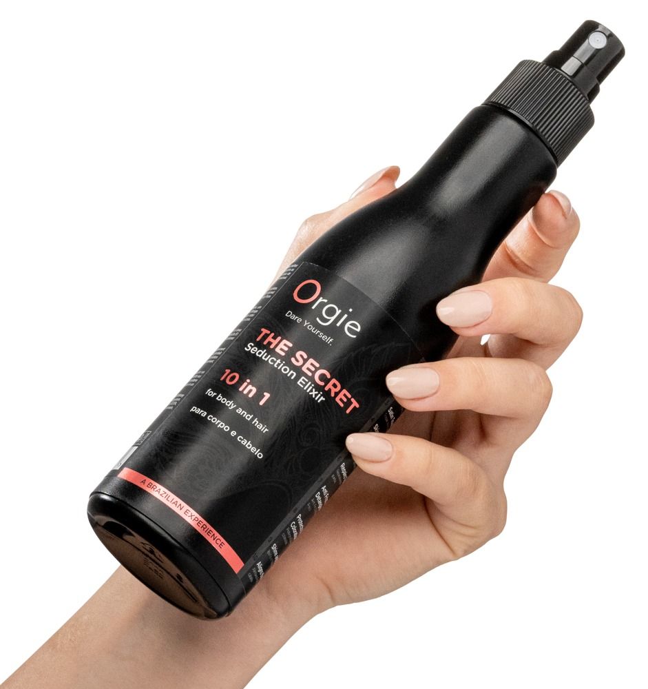 Flacone nero tenuto in mano. Nome prodotto: Orgie - The Secret Seduction Elixir. Testo: 10 in 1, per corpo e capelli.