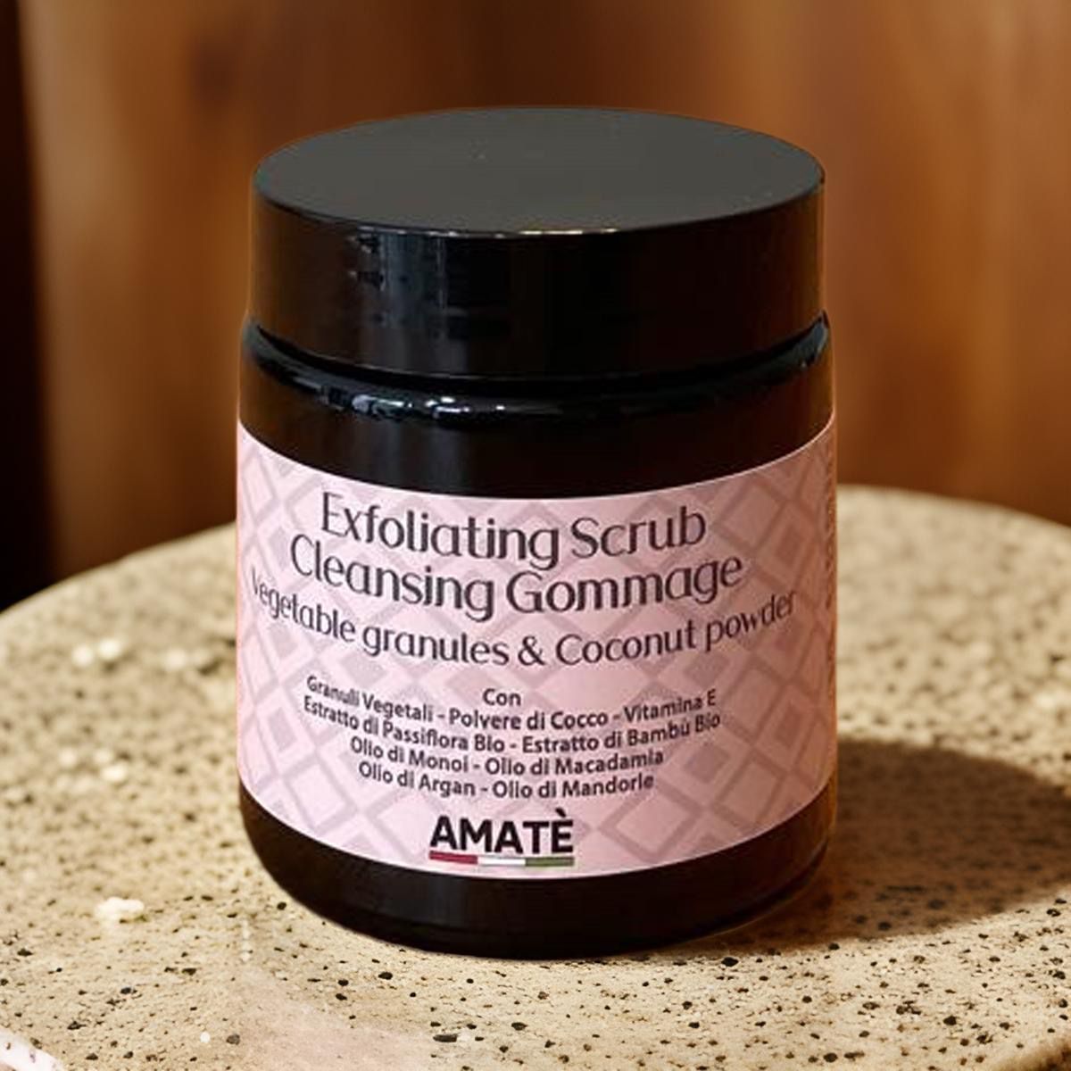 Barattolo scuro con etichetta. Testo: Exfoliating Scrub Cleansing Gommage, Vegetable granules & Coconut powder. Marchio: AMATÈ. Su una piastra.