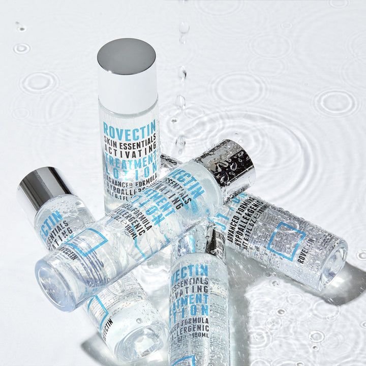 Diversi flaconi ROVECTIN Skin Essentials Activating Treatment Lotion, parzialmente coperti da gocce d'acqua. Tappi argentati.