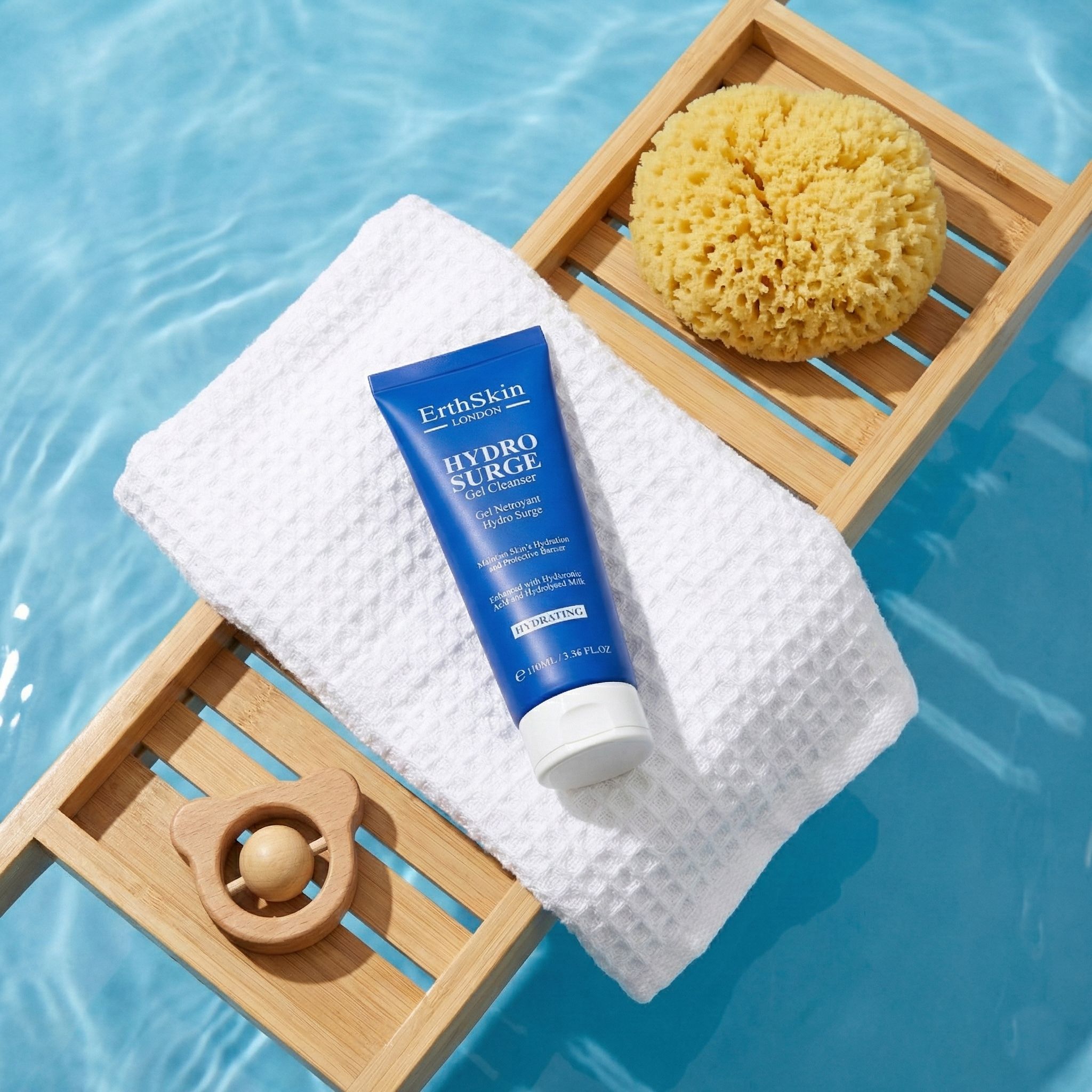 Tubo blu con testo. Su asciugamano bianco, vassoio in legno con spugna e giocattolo. Sfondo d'acqua.