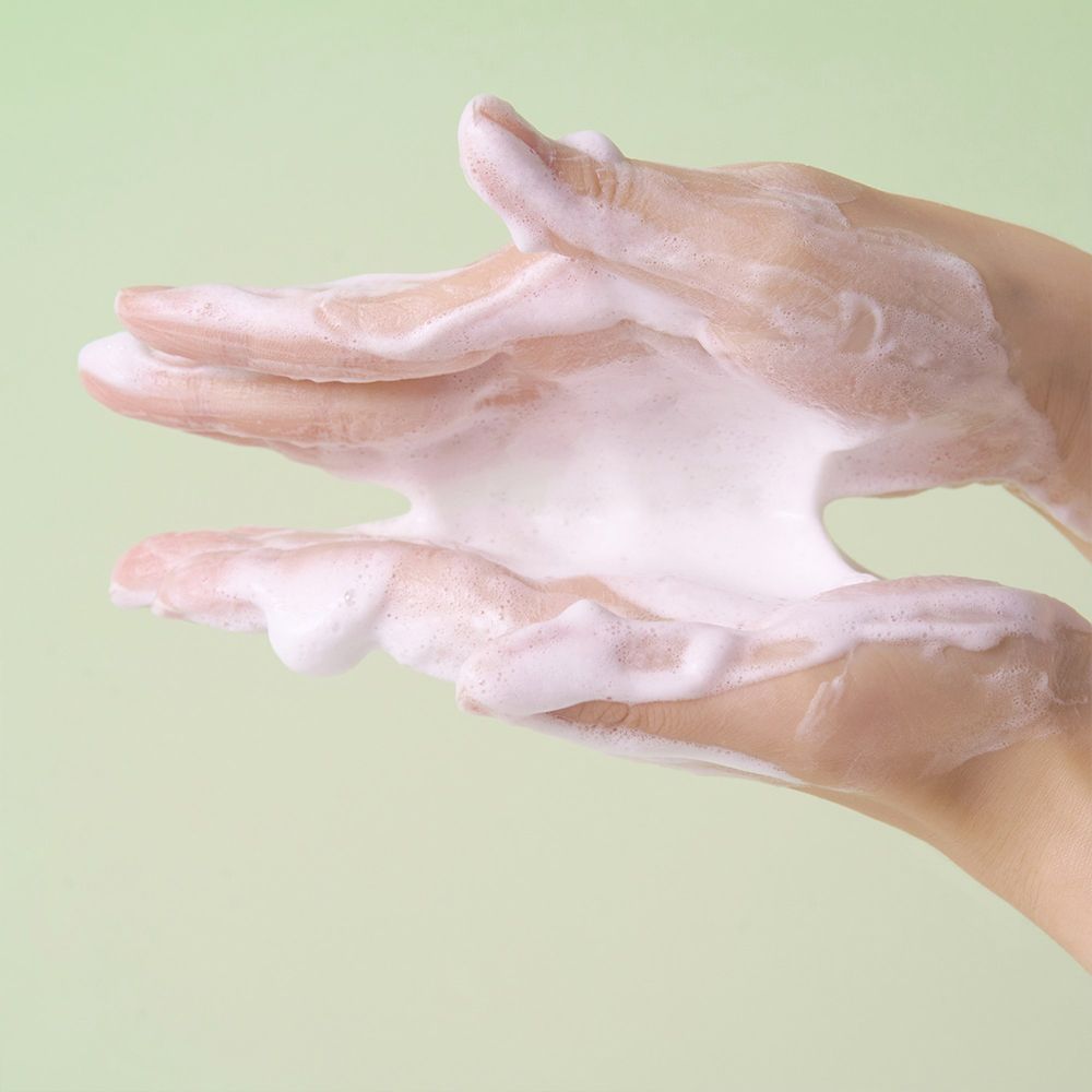 Mani con prodotto detergente schiumoso che fuoriesce tra le dita.