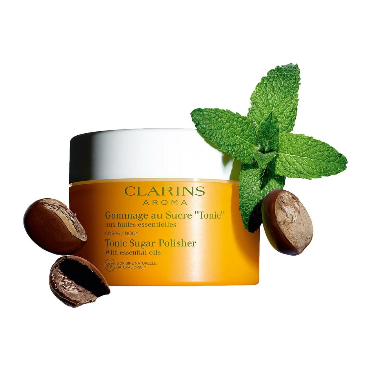Vasetto giallo con coperchio bianco. Accanto foglie e noci. Scritta: Clarins Aroma, Gommage au Sucre Tonic, Tonic Sugar Polisher.