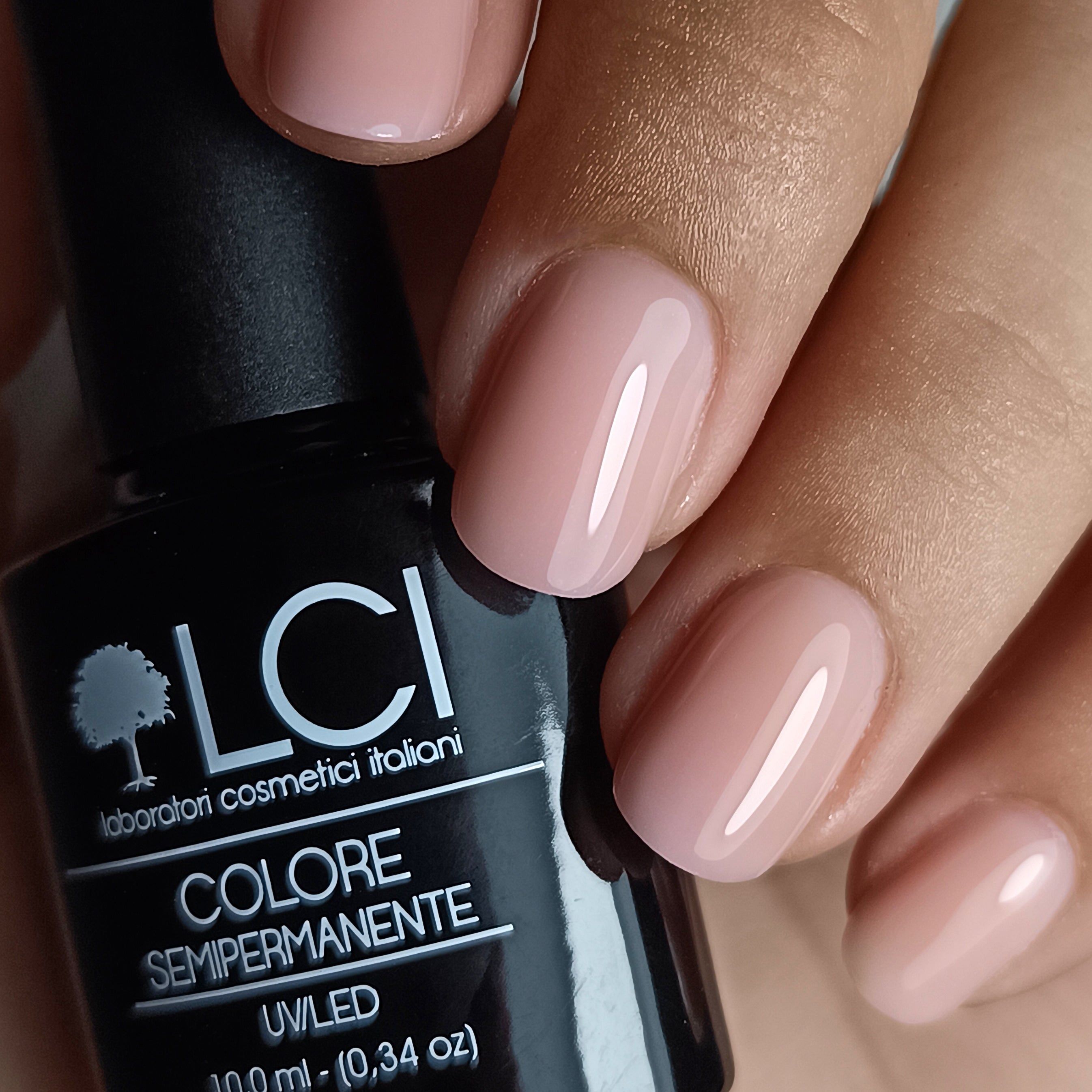 Flacone di smalto e unghie smaltate. Flacone con tappo nero, etichetta con testo. Unghie rosa.