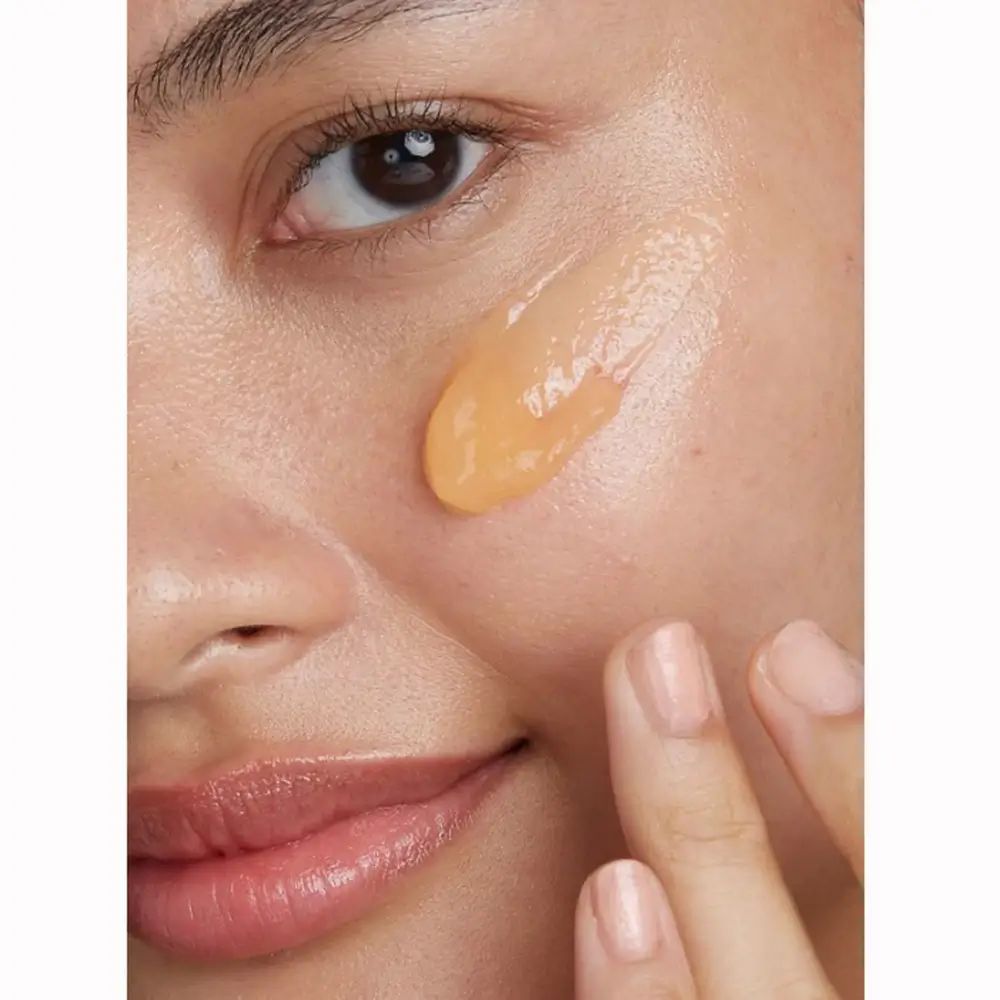 Primo piano di una persona con un gel giallo sulla pelle. Le dita toccano la pelle. La pelle è liscia e uniforme.