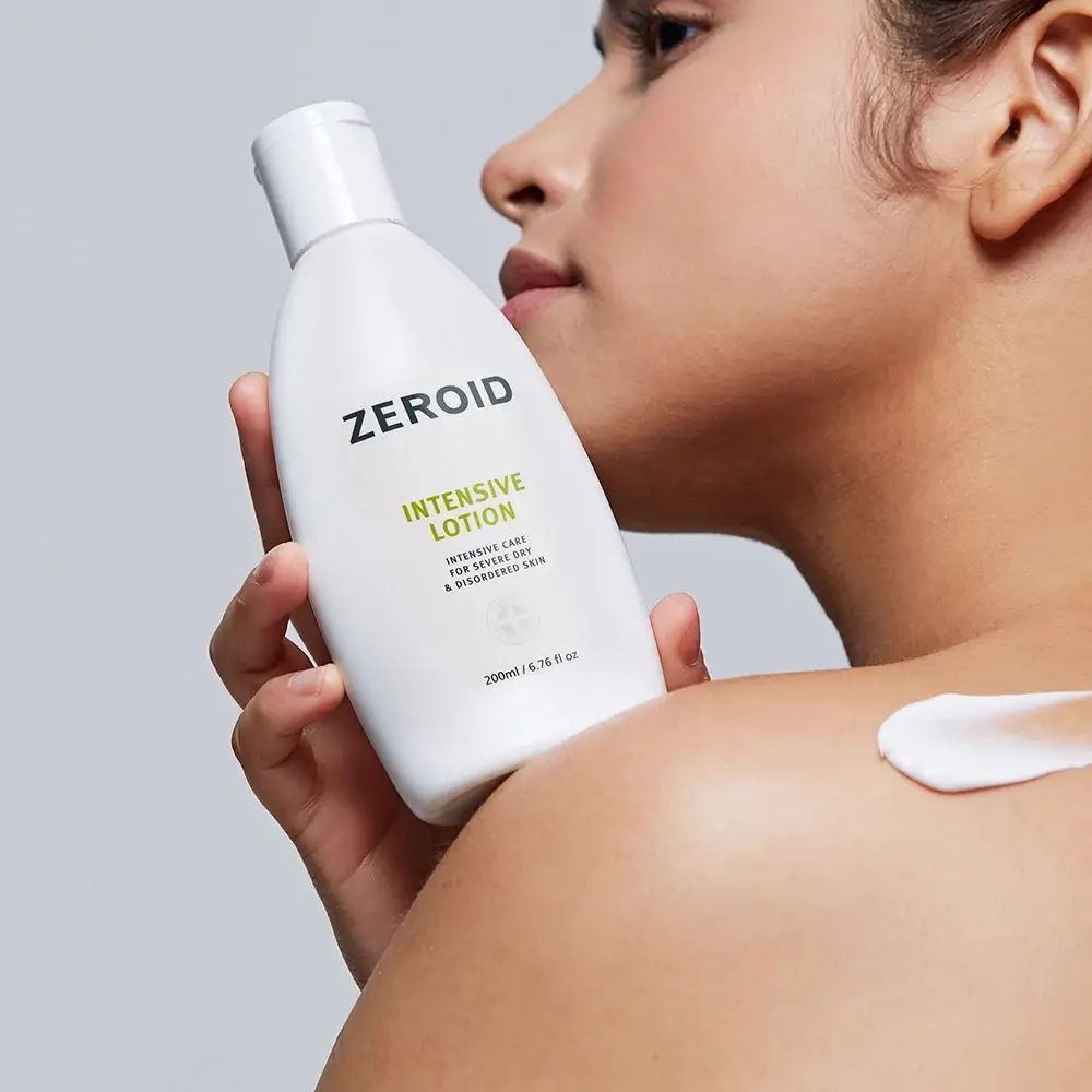 Persona che tiene in mano un flacone di ZEROID Intensive Lotion. Crema applicata sulla spalla. Testo verde.
