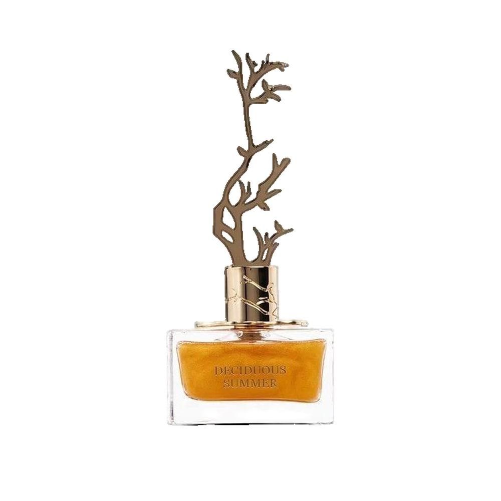 Flacone rettangolare in vetro con liquido dorato. Tappo dorato a forma di albero. Scritta: DECIDUOUS SUMMER.