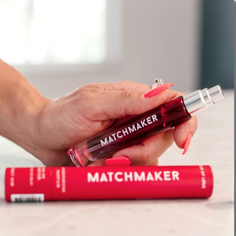 Persona che tiene in mano un flacone di profumo rosso "MATCHMAKER" e la confezione. Unghie rosse.