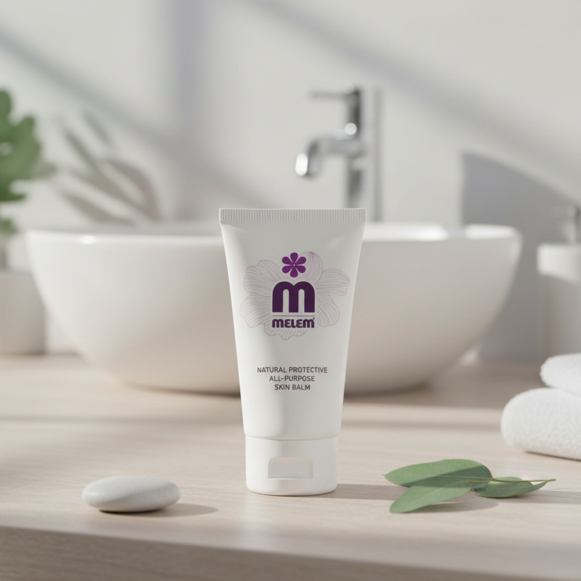 Tubetto bianco con logo viola e testo: Melem, Natural Protective All-Purpose Skin Balm. Posizionato davanti a un lavandino.