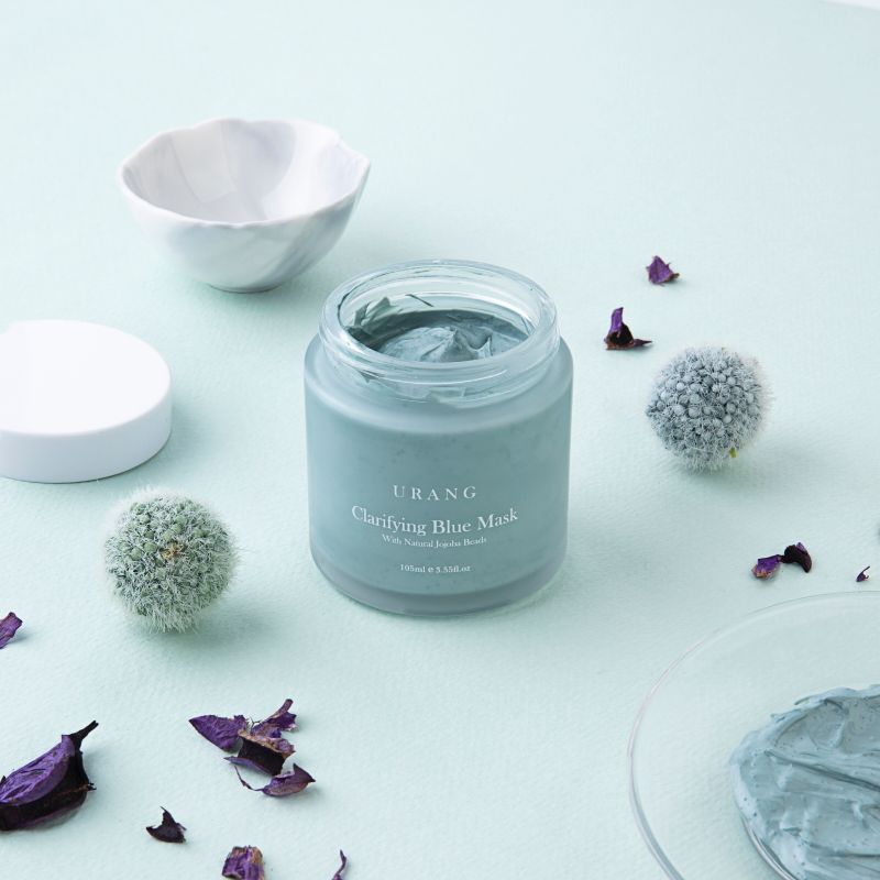 Vaso aperto con crema blu, petali e accessori. Scritta: URANG Clarifying Blue Mask.