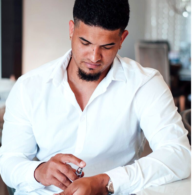 Un uomo è seduto e spruzza profumo sul polso. Scritta: EYE OF LOVE Pheromone Parfum Romantic.