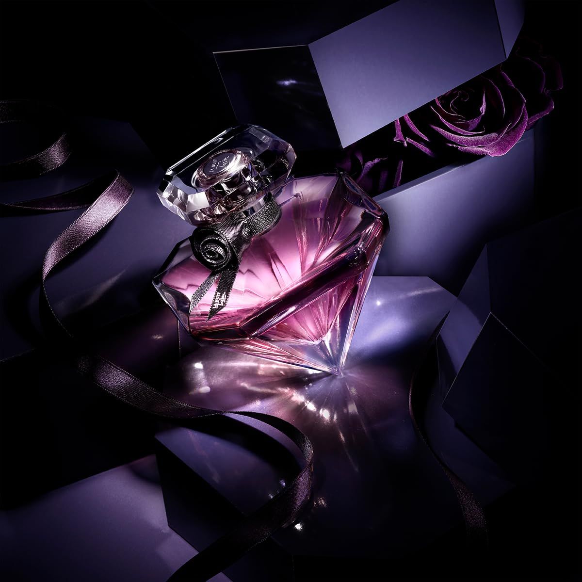 Flacone di profumo con fiocco nero, accanto a una scatola aperta con rose.