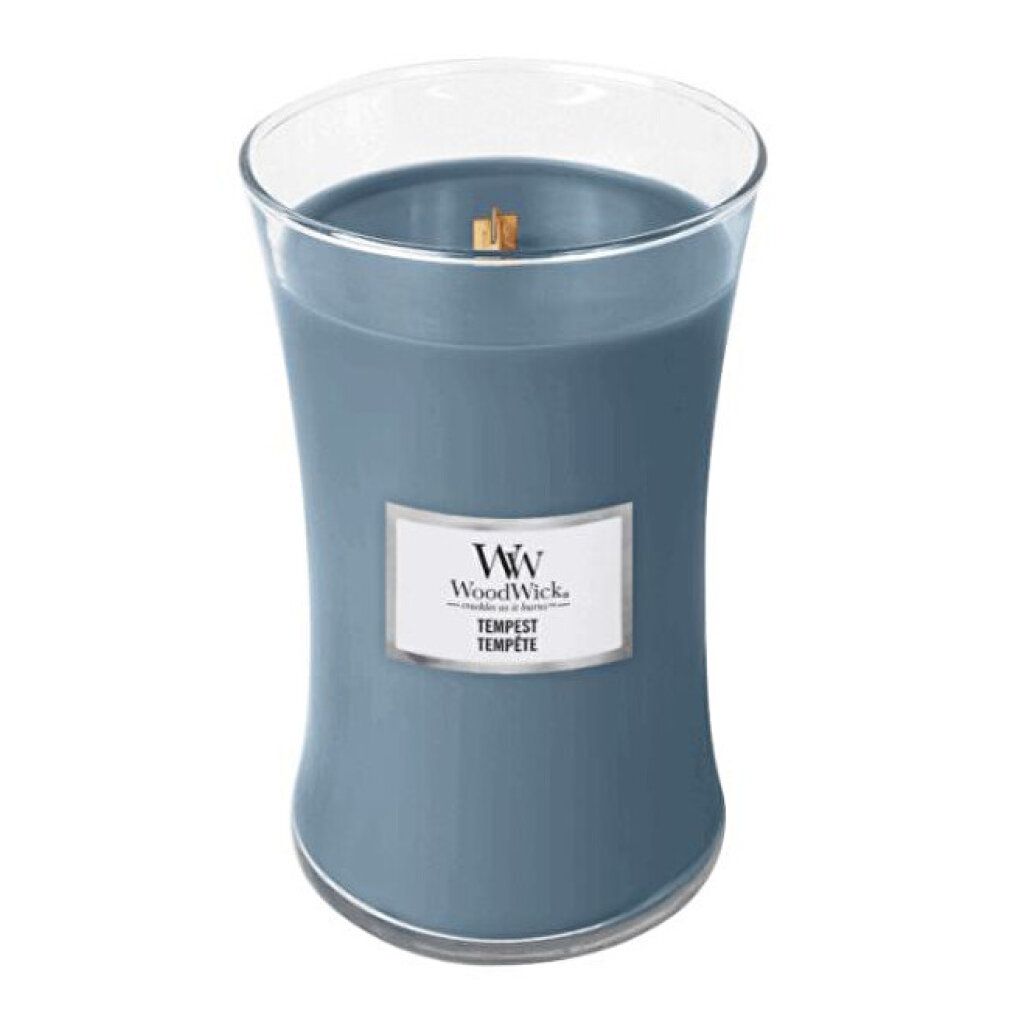 Candela blu in contenitore di vetro. Etichetta con logo e scritta Tempest. Stoppino in legno visibile.
