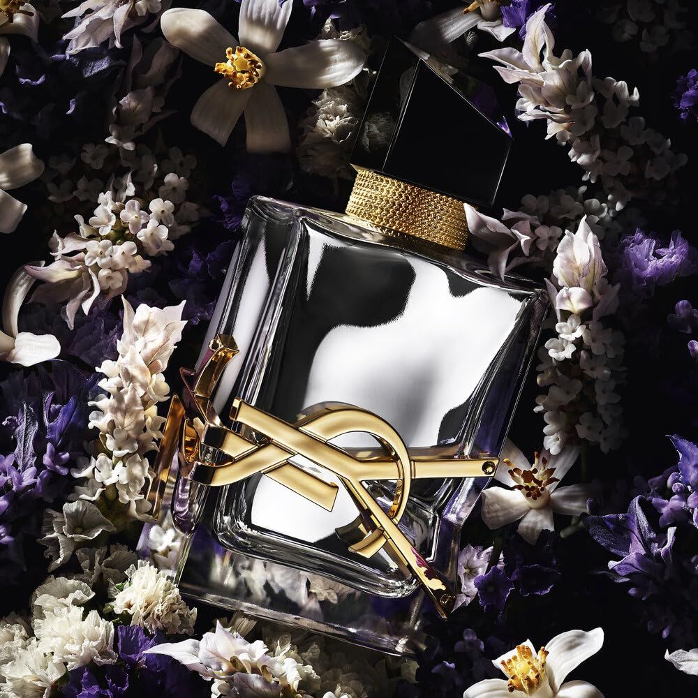 Flacone di profumo. Flacone quadrato in vetro con logo dorato e tappo nero. Circondato da fiori.