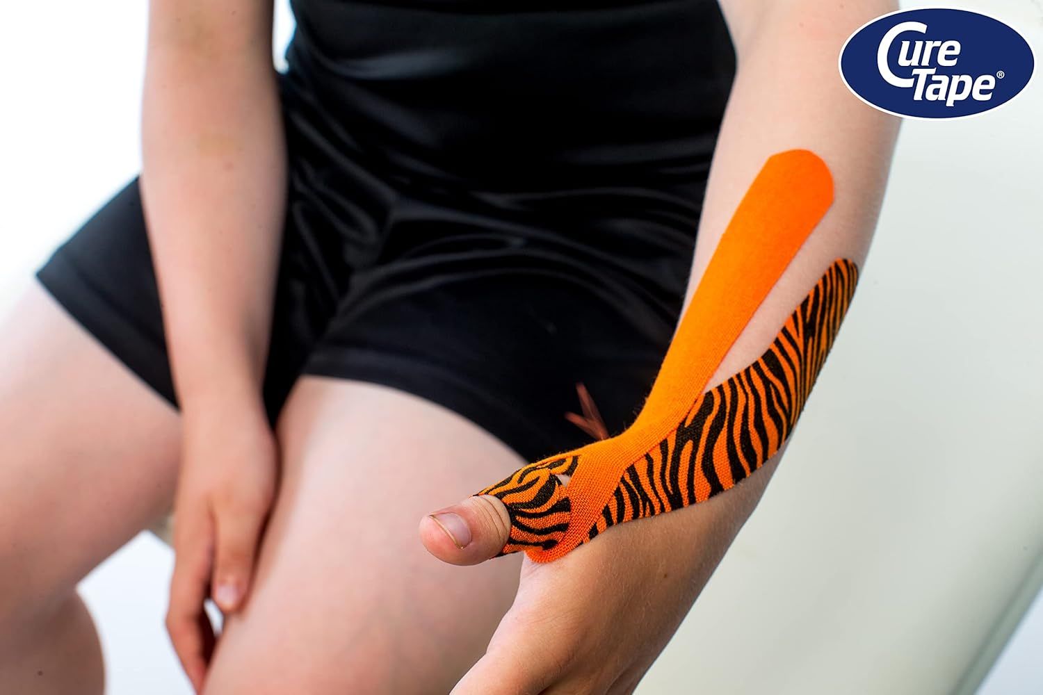 Braccio con CureTape Tiger. Arancione e nero. Tape applicato sul braccio. Logo CureTape visibile.