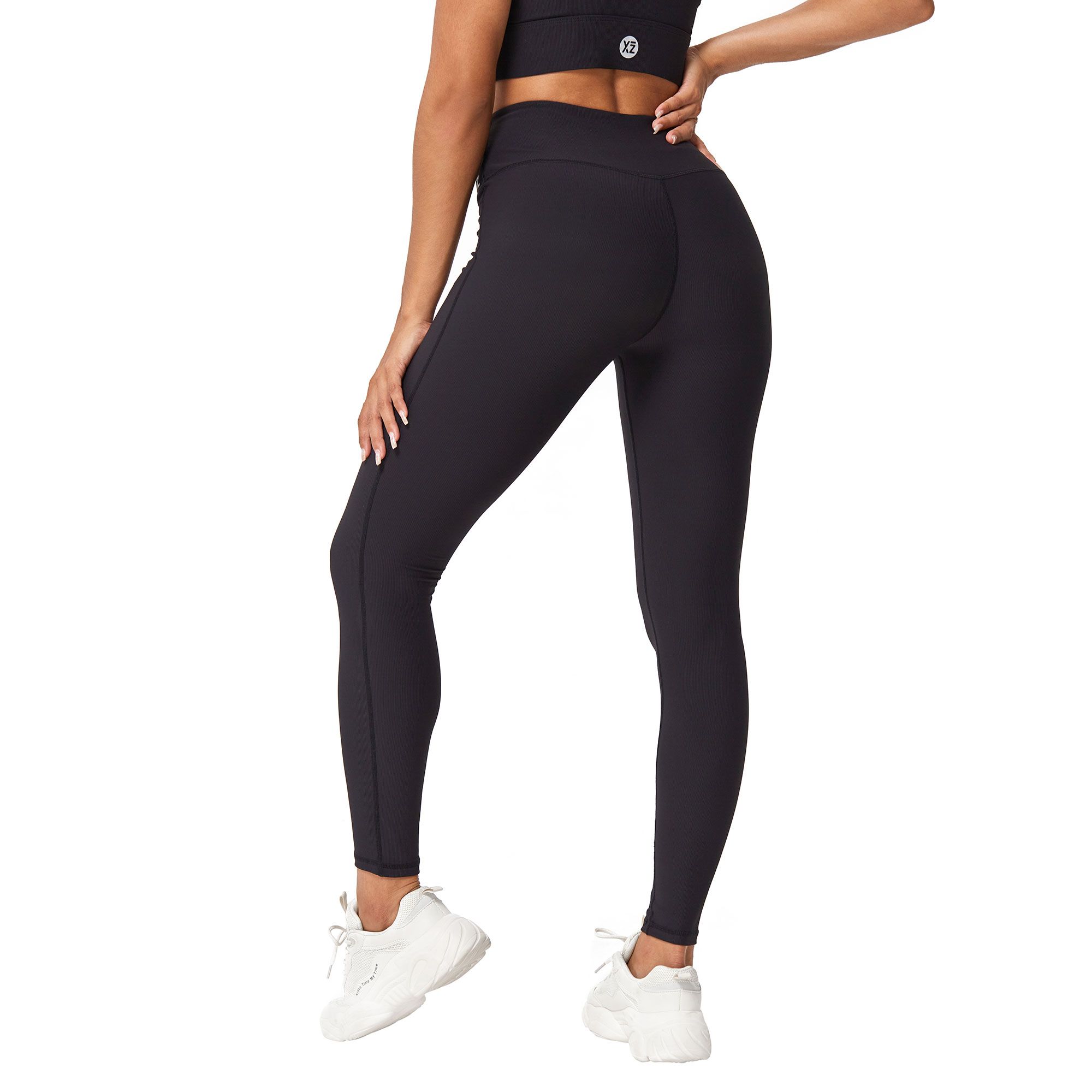 Leggings neri aderenti con un piccolo logo in vita. Sfondo bianco.