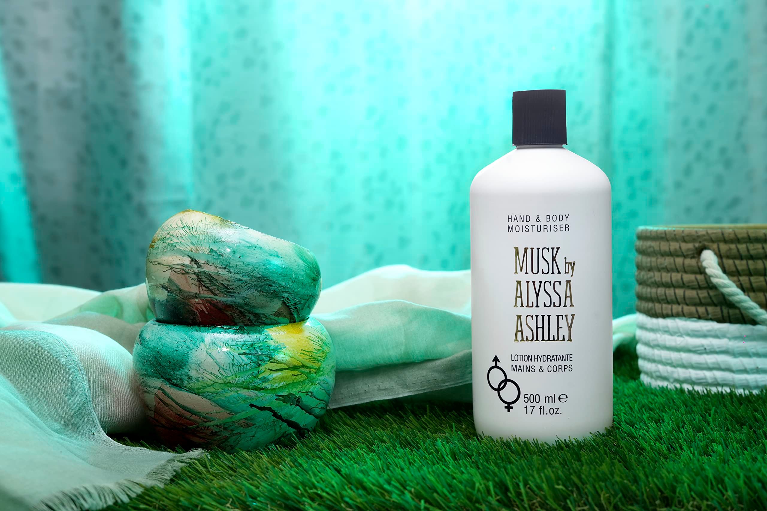 Flacone bianco con tappo nero. Scritta: Musk by Alyssa Ashley, Hand & Body Moisturiser. Posizionato sull'erba.