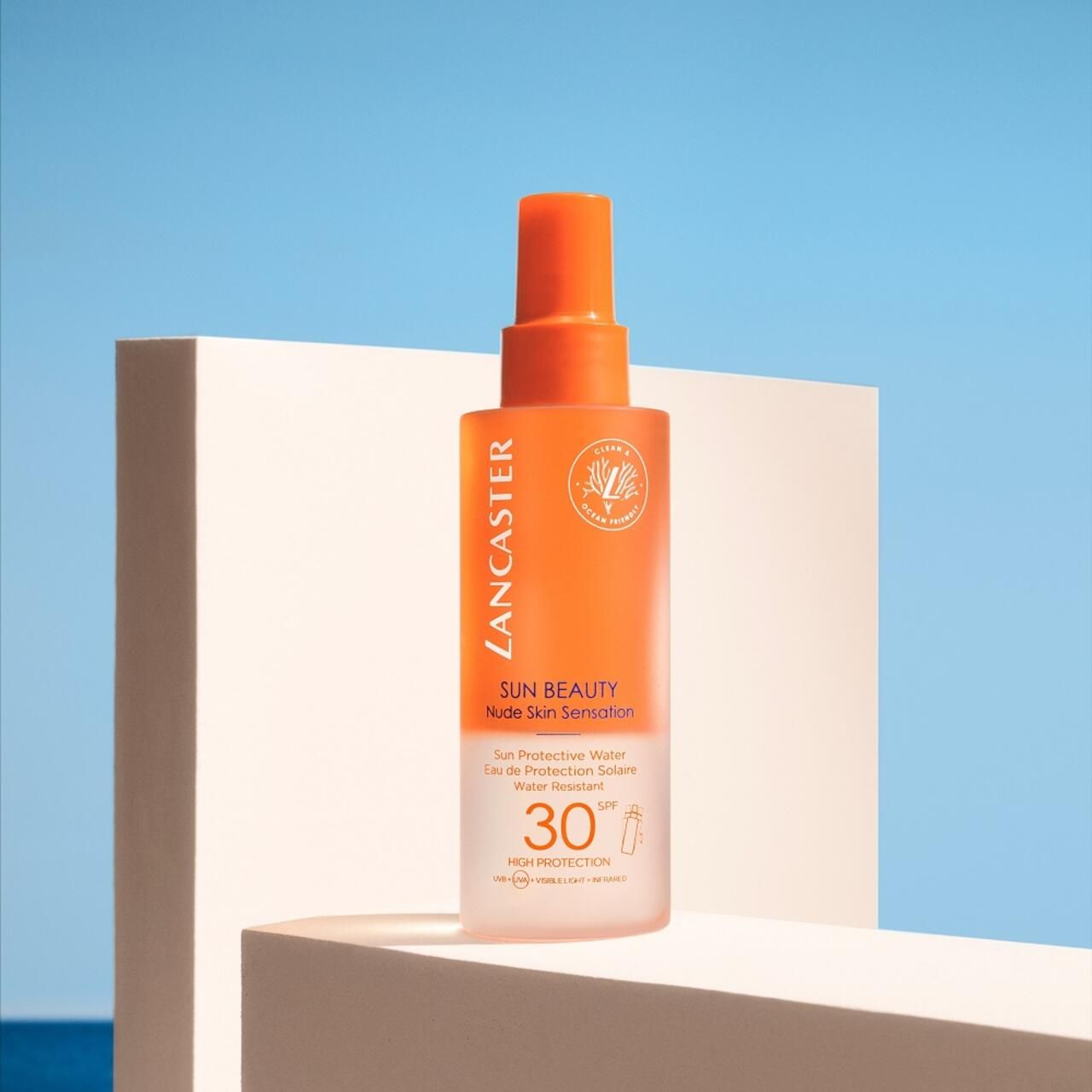 Lancaster Sun Beauty Protective Water SPF30. Flacone arancione su piedistallo bianco. Testo: Nude Skin Sensation, SPF 30.