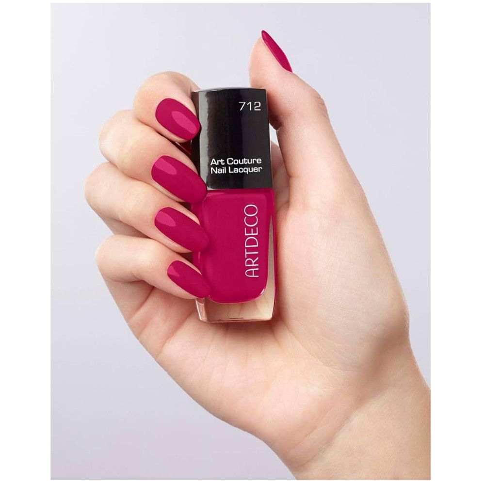 Mano che tiene una bottiglia di smalto rosa. Lo smalto e le unghie sono rosa. Sulla bottiglia c'è scritto Artdeco e Art Couture Nail Lacquer.