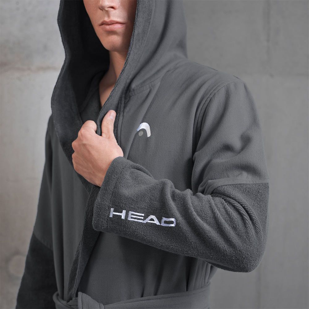 Accappatoio grigio con cappuccio. Logo e scritta HEAD sulla manica. Uomo che indossa l'accappatoio. Sfondo grigio.