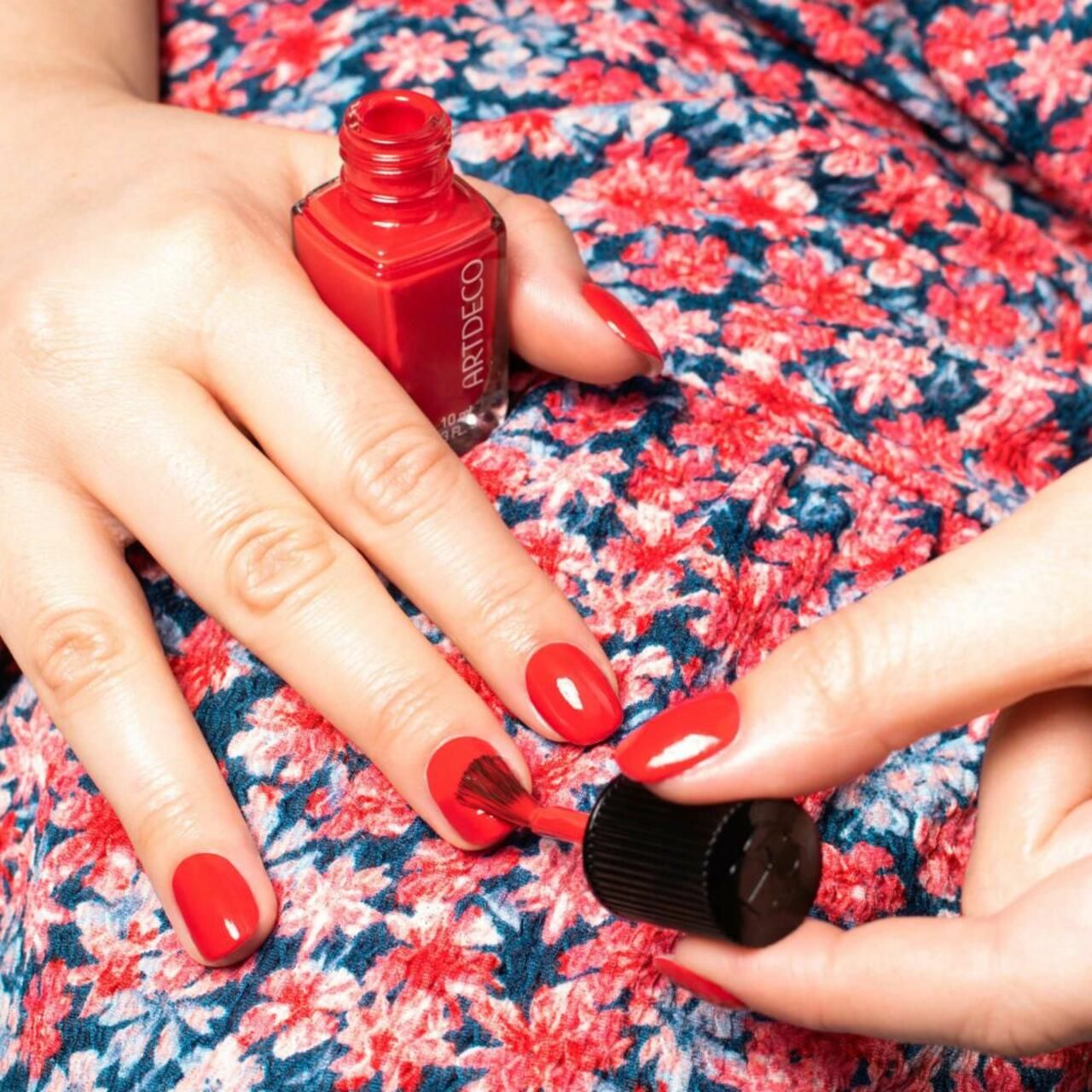 Persona che smalta le unghie rosse con Artdeco Quick Dry Nail Lacquer. Flacone con tappo nero. Scritta: Quick Dry Nail Lacquer, Vernis à ongles.