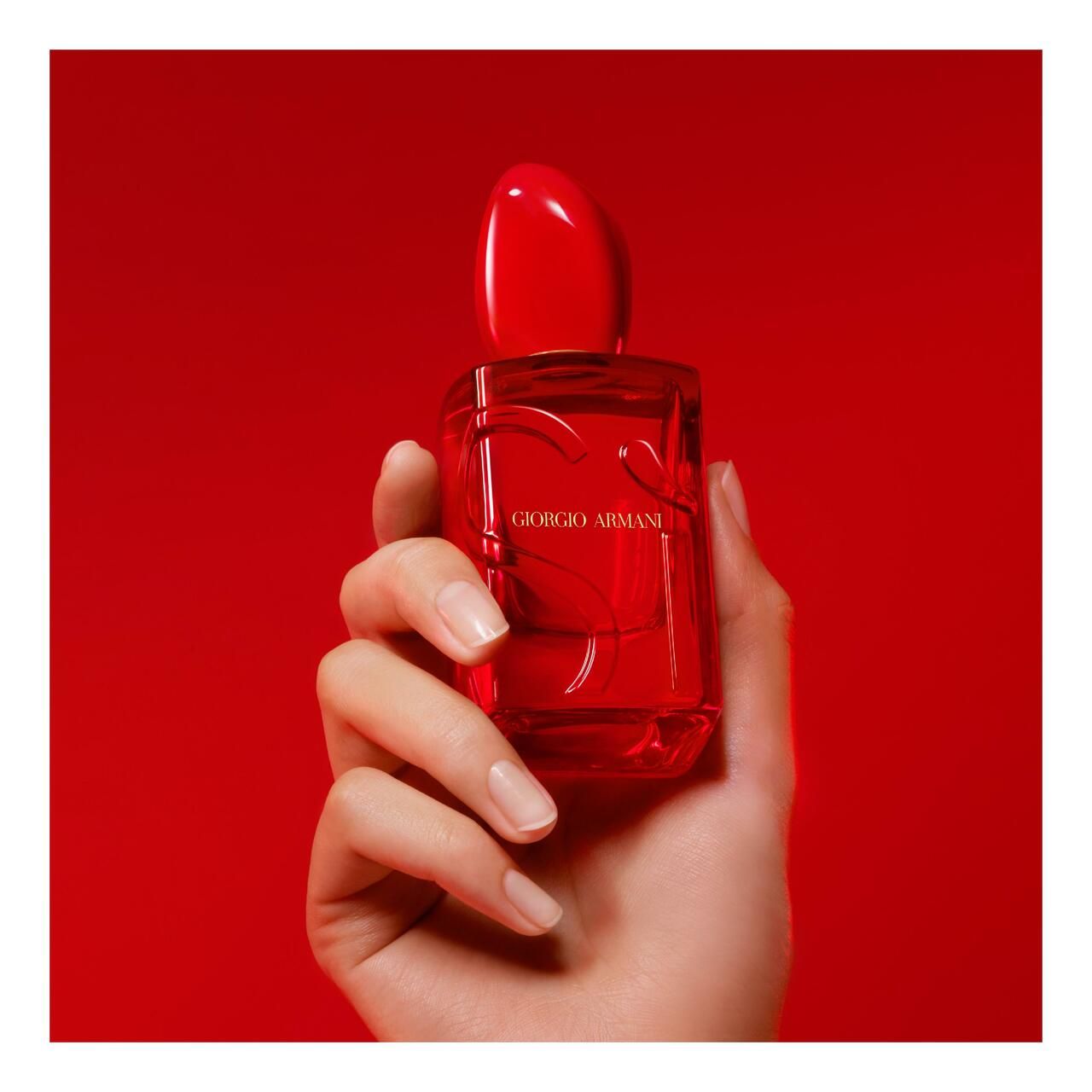 Flacone rosso Giorgio Armani Sì Passione Red Musk in una mano su sfondo rosso.