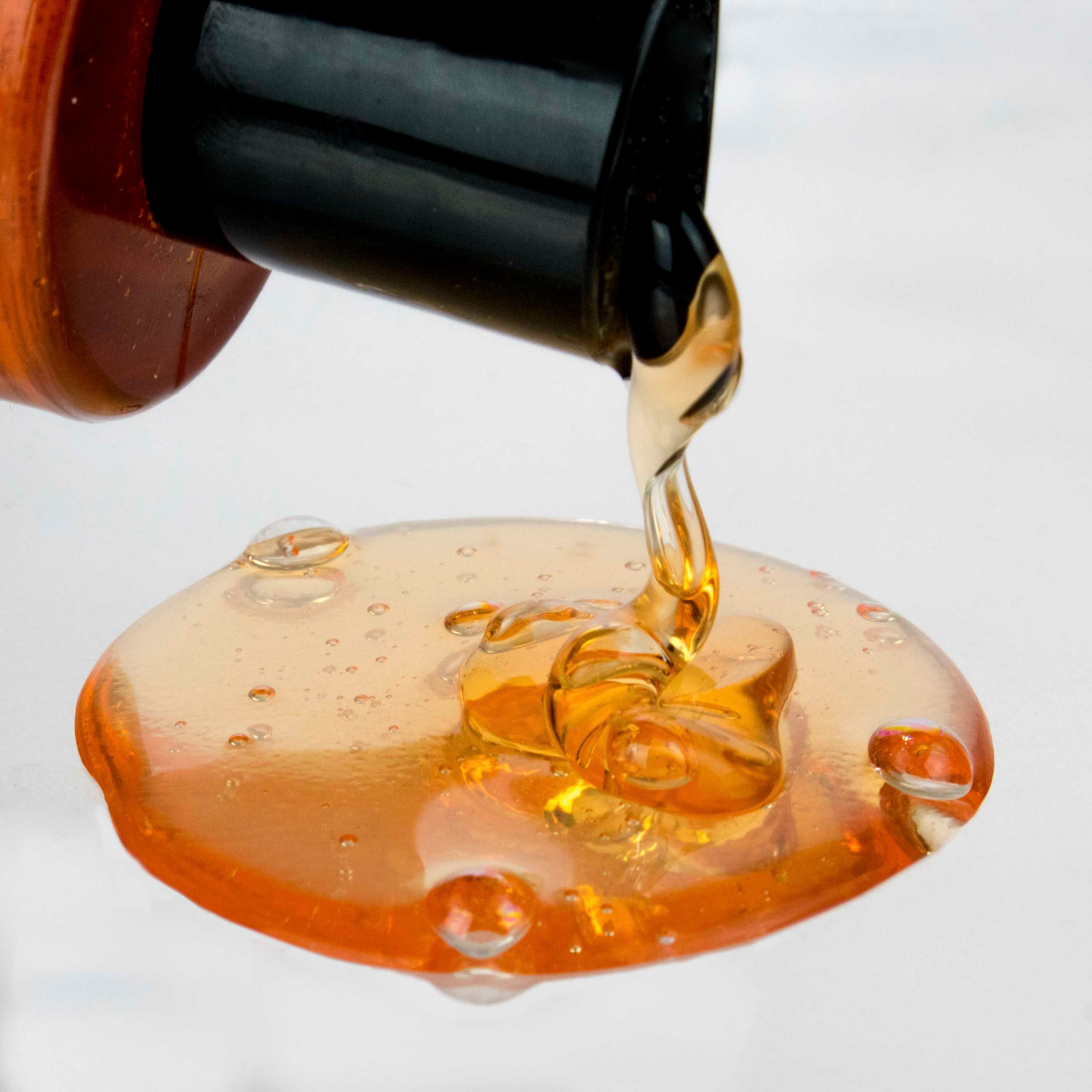 Shampoo all'olio di argan che cola. Liquido marrone. Su sfondo chiaro. Nome del prodotto non visibile.