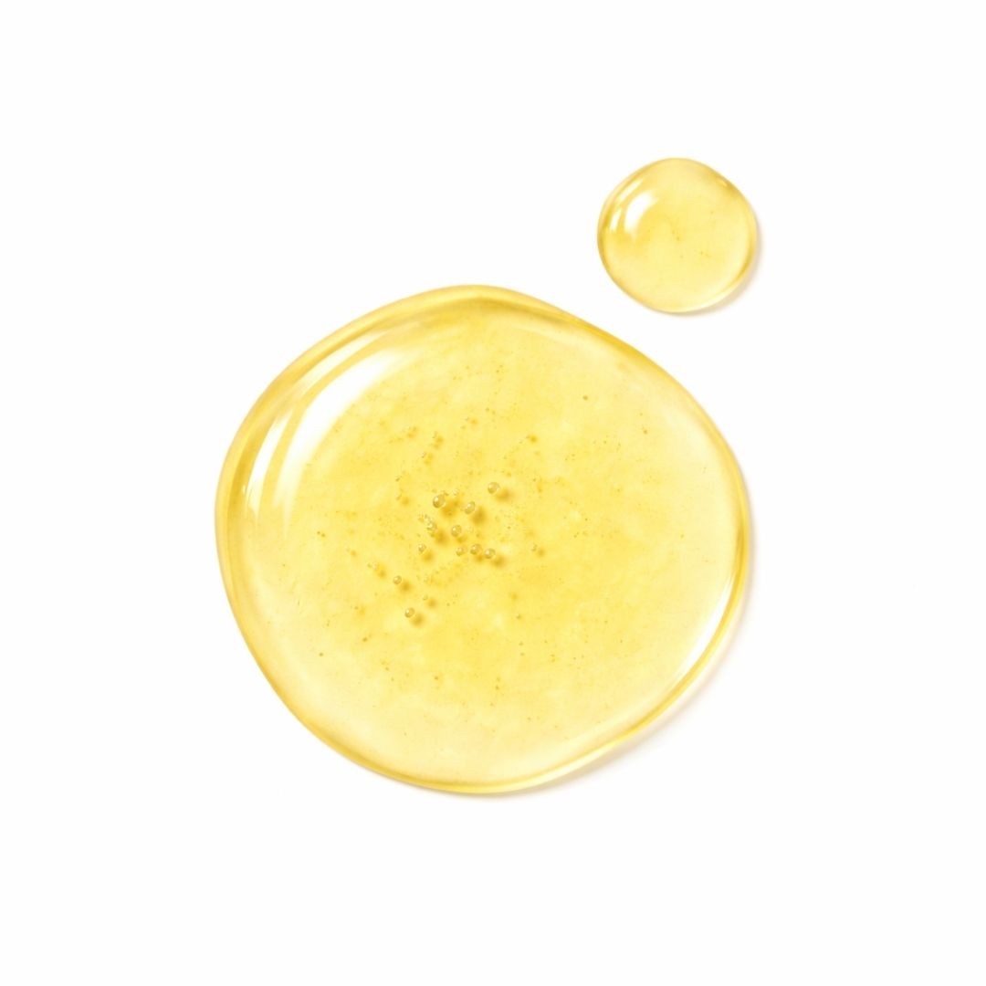 Due gocce di liquido giallo su sfondo bianco. La goccia più grande ha delle bolle.