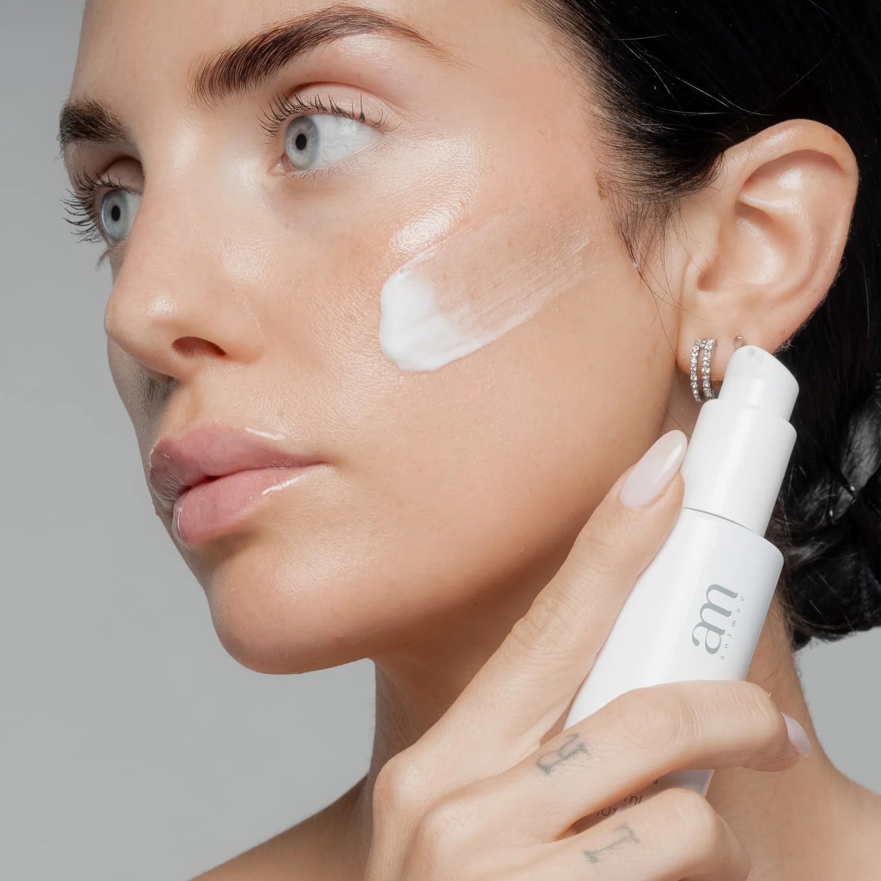 Donna che applica il siero sul viso. Flacone bianco con logo AM. Pelle coperta di siero.