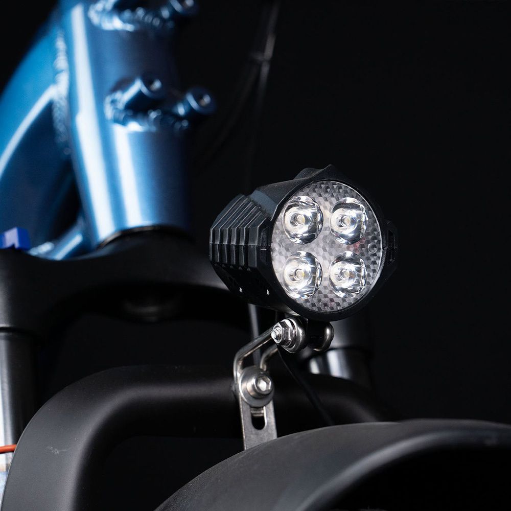 Primo piano del faro anteriore di una e-bike blu. Quattro luci LED in un alloggiamento nero.