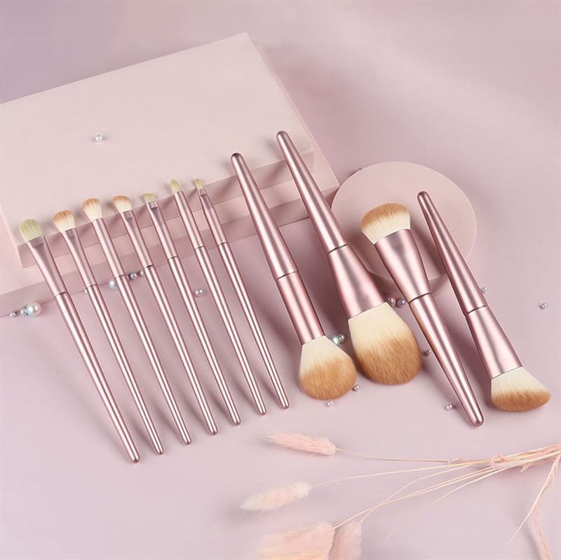 Set di pennelli per trucco. Manici rosa, setole chiare. Varie forme e dimensioni. Su sfondo rosa.