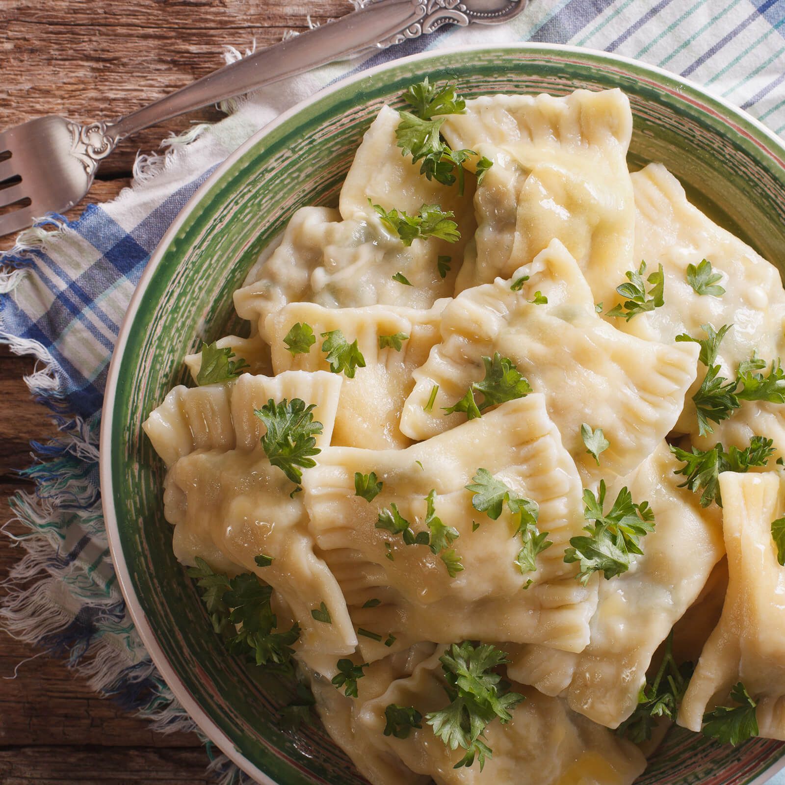 Ciotola di ravioli, guarniti con prezzemolo. Su un tavolo con forchetta e tovagliolo.
