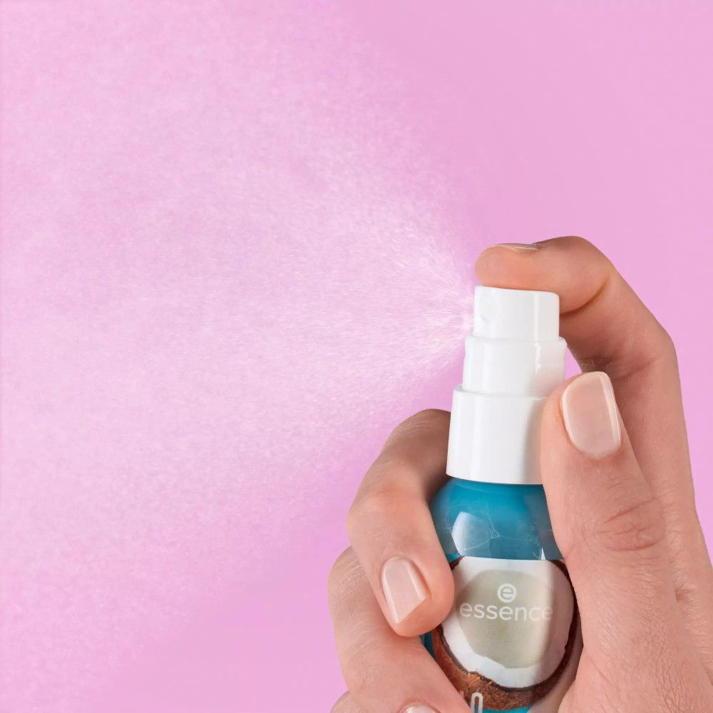 Mano che tiene un flacone spray. L'erogatore viene azionato, la nebulizzazione è visibile. Sfondo: rosa.