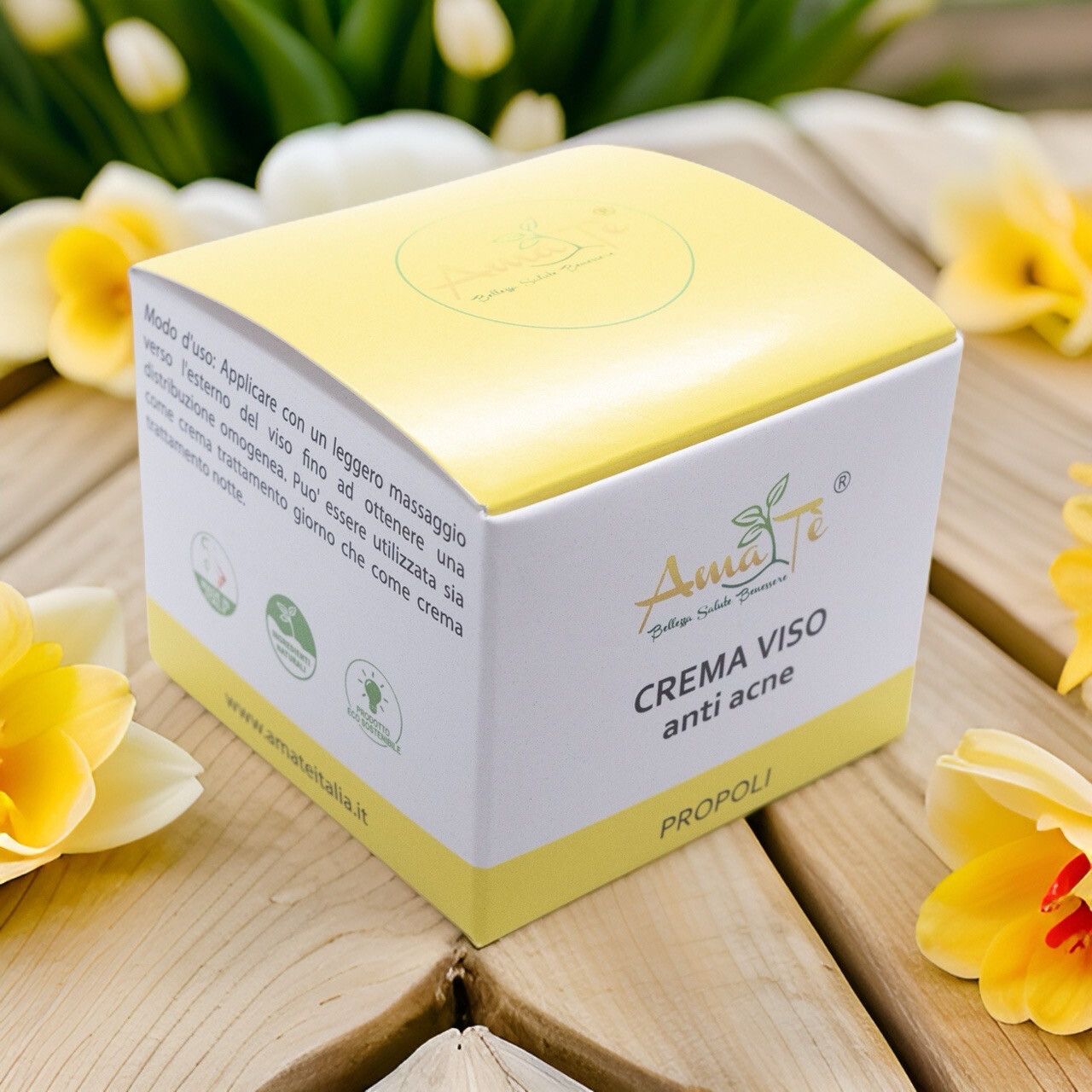 Scatola bianca e gialla su superficie in legno con fiori. Scritto: Crema viso anti acne, Propoli. Logo con foglie. Fiori gialli.