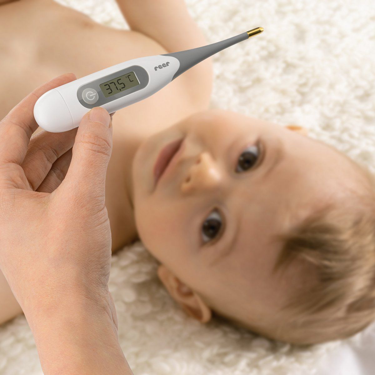 Un termometro viene utilizzato su un bambino. Il termometro mostra 37,5°C. Marchio: reer.