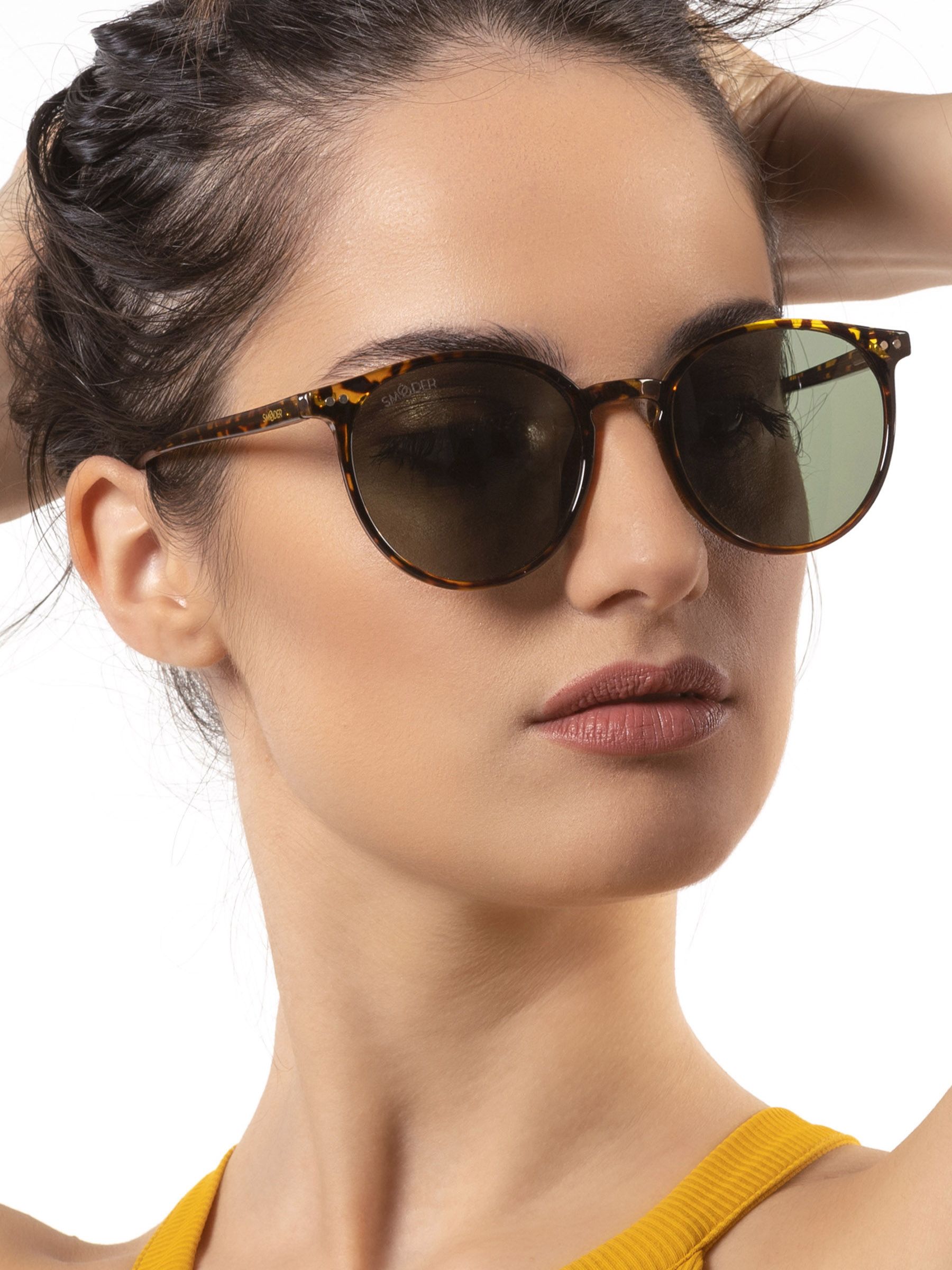 Donna con occhiali da sole rotondi, motivo tartarugato marrone, lenti verdi. Marchio Smooder.