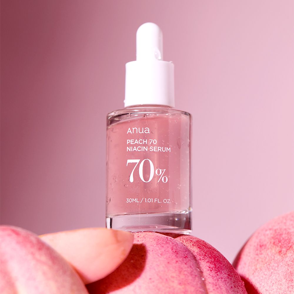 Flacone di siero Anua Peach 70 Niacin su pesche, sfondo rosa.